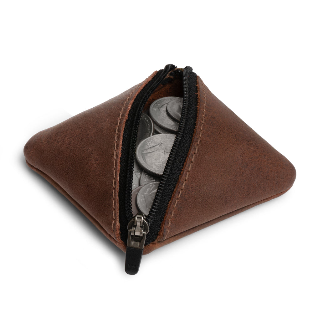 Slash Zippered Pouch by Hide & Drink, demonstrated with coins spilling out to show its functionality as a change holder. Made of durable full grain leather, this artisan piece supports pocket and purse organization and is crafted in La Antigua Guatemala & Oaxaca Mexico.