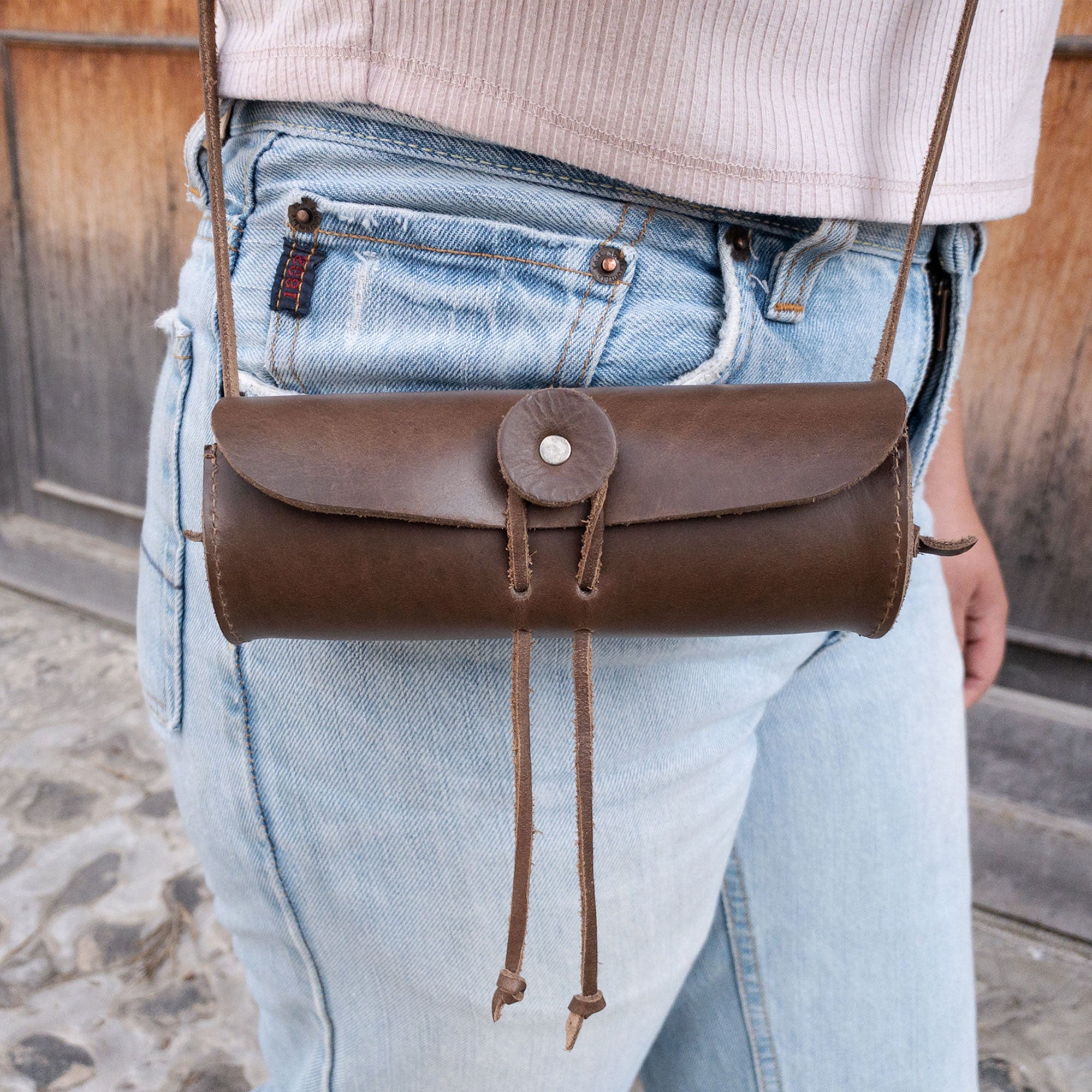 A model wearing the La Antigua Spotting Scope Case, showcasing its stylish design as a rustic storage case. This artisan-crafted case serves as a protective sleeve for your spotting scope and is made from high-quality full grain leather. Perfect for travel and outdoor use, it's a small batch production piece from La Antigua, Guatemala.