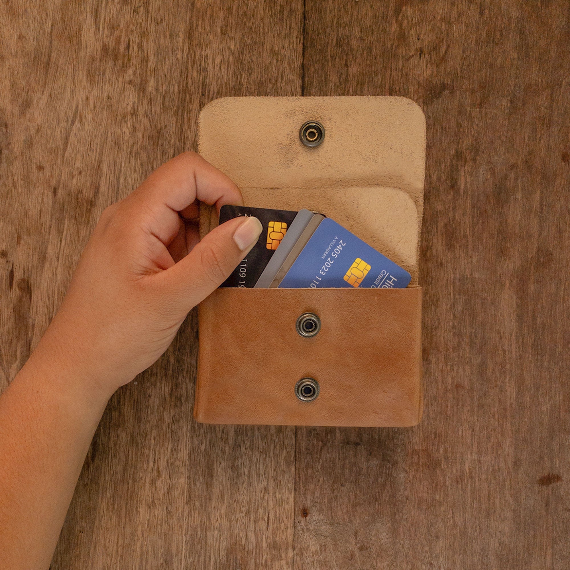A hand retrieving a card from the brown Double Pouch Card Wallet by Hide & Drink. This Leather Double Pouch Card Wallet serves as a practical card organizer, cash holder, or coin pouch, ideal for both men and women, made from Full Grain Leather in La Antigua Guatemala & Oaxaca Mexico.