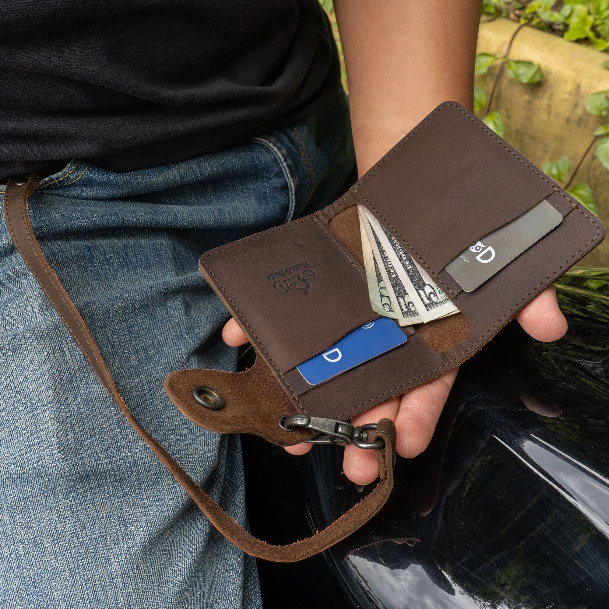 Hide & Ride Biker Wallet in use, held by a biker. This rectangular wallet is a compact wallet with a belt loop and strap, showcasing its functionality as a card holder with snap closure.