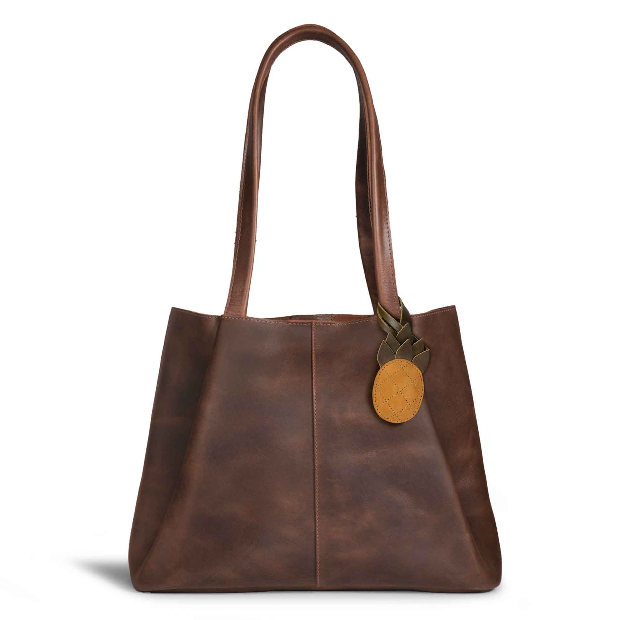 Hide & Drink Bag Charms attached to a chic brown handbag, featuring a stylish leaf design, perfect for personalization. This accessory serves as a purse charm for tote & backpacks crafted from quality full grain leather. Every piece reflects StockyardX's commitment to small batch production, showcasing hand cut, hand sewn artistry along with fire branding, handmade in La Antigua Guatemala & Oaxaca Mexico.