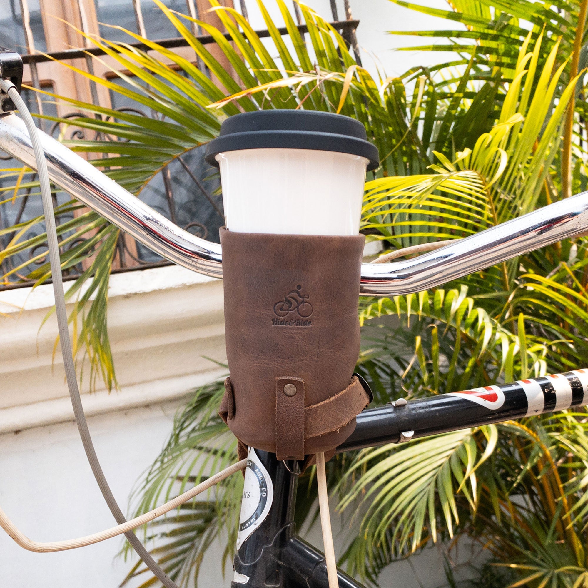 Cruzy Bike Handlebar Cup Holder by Hide & Ride mounted on a bicycle, showcasing the full grain leather material. This insulated beverage pouch is perfect for commuters and cyclists, handcrafted by artisans in La Antigua Guatemala for durability and style.