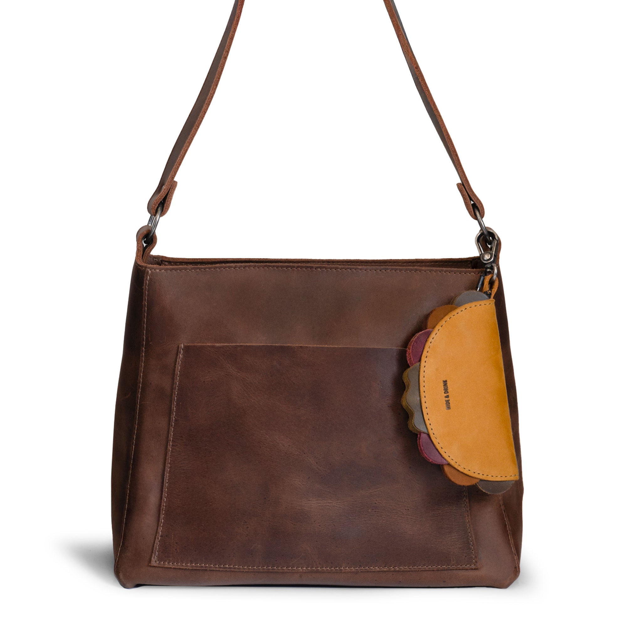 Hide & Drink Taco Zip Pouch Bag Charm Key Chain attached to a brown leather shoulder bag, showcasing its tan taco-shaped design and convenient clip. Taco Zip Pouch Bag Charm Key Chain Full Grain Leather, StockyardX, Small Batch Production, Hand Cut, Hand Sewn, Fire Branded, Artisan, Handmade in La Antigua Guatemala & Oaxaca Mexico.