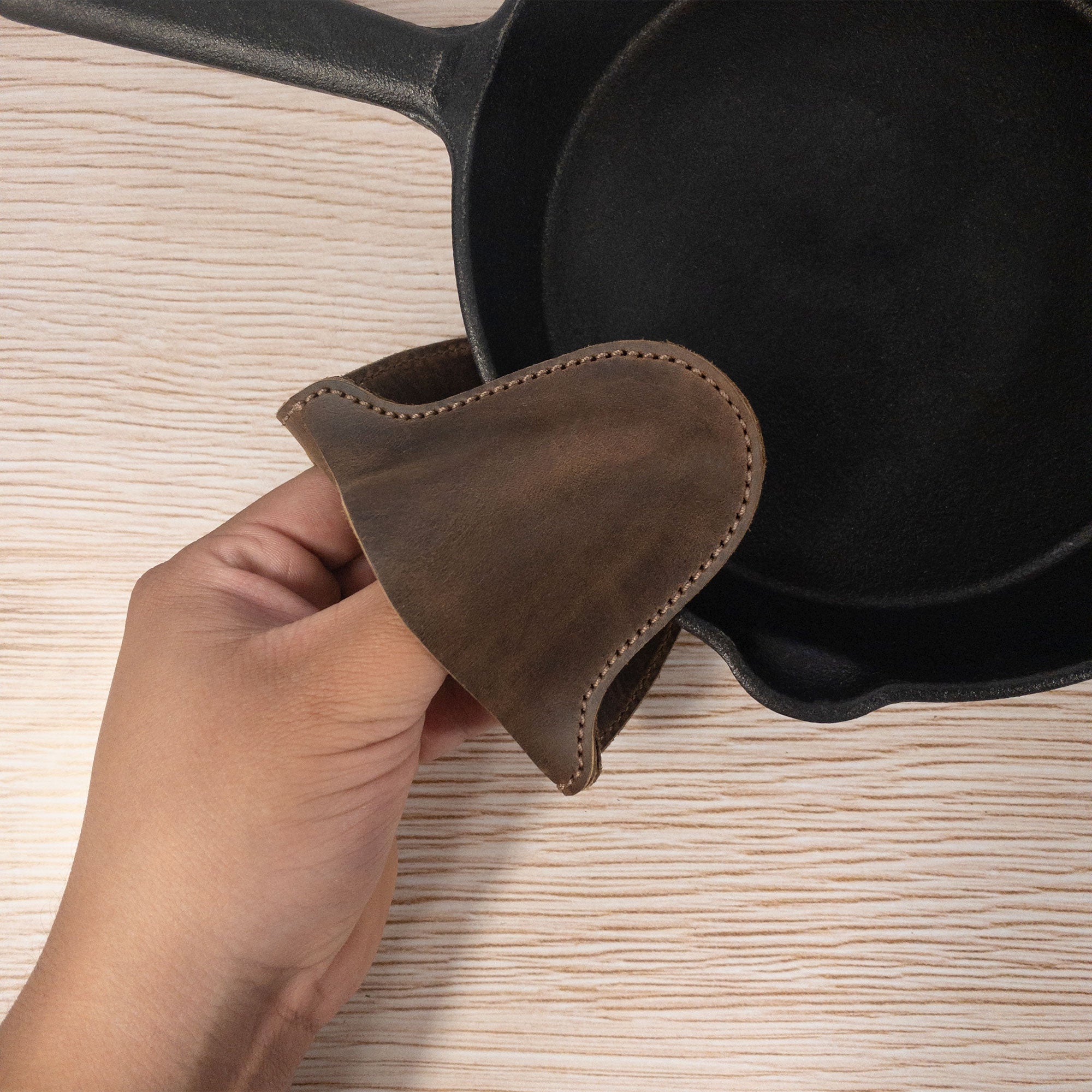 Close-up of the Oven Mitt Heat Resistant by Cast Leather Co., being used to handle a hot cast iron skillet. This full grain leather oven glove is designed for kitchen cooking and baking, reflecting artisan craftsmanship with a rustic charm. Handmade in La Antigua Guatemala, it combines functionality with artistry.