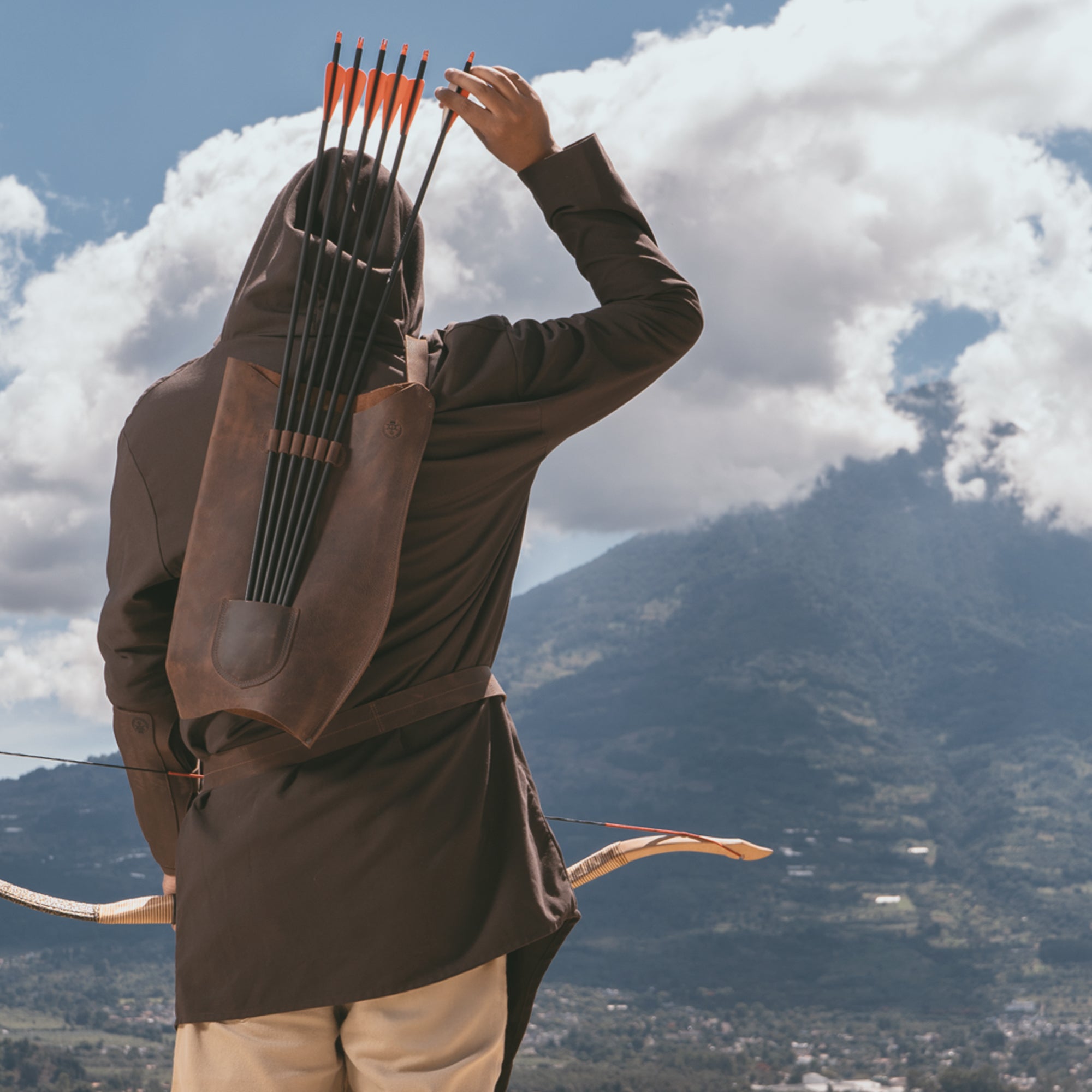 Archer wearing Valhalla Gear's Archery Bow Carrier with Arrow Slots in a scenic outdoor setting. This carrier, crafted from full grain leather, combines adjustable features and artisan craftsmanship, perfect for shooting, training, or cosplay adventures.