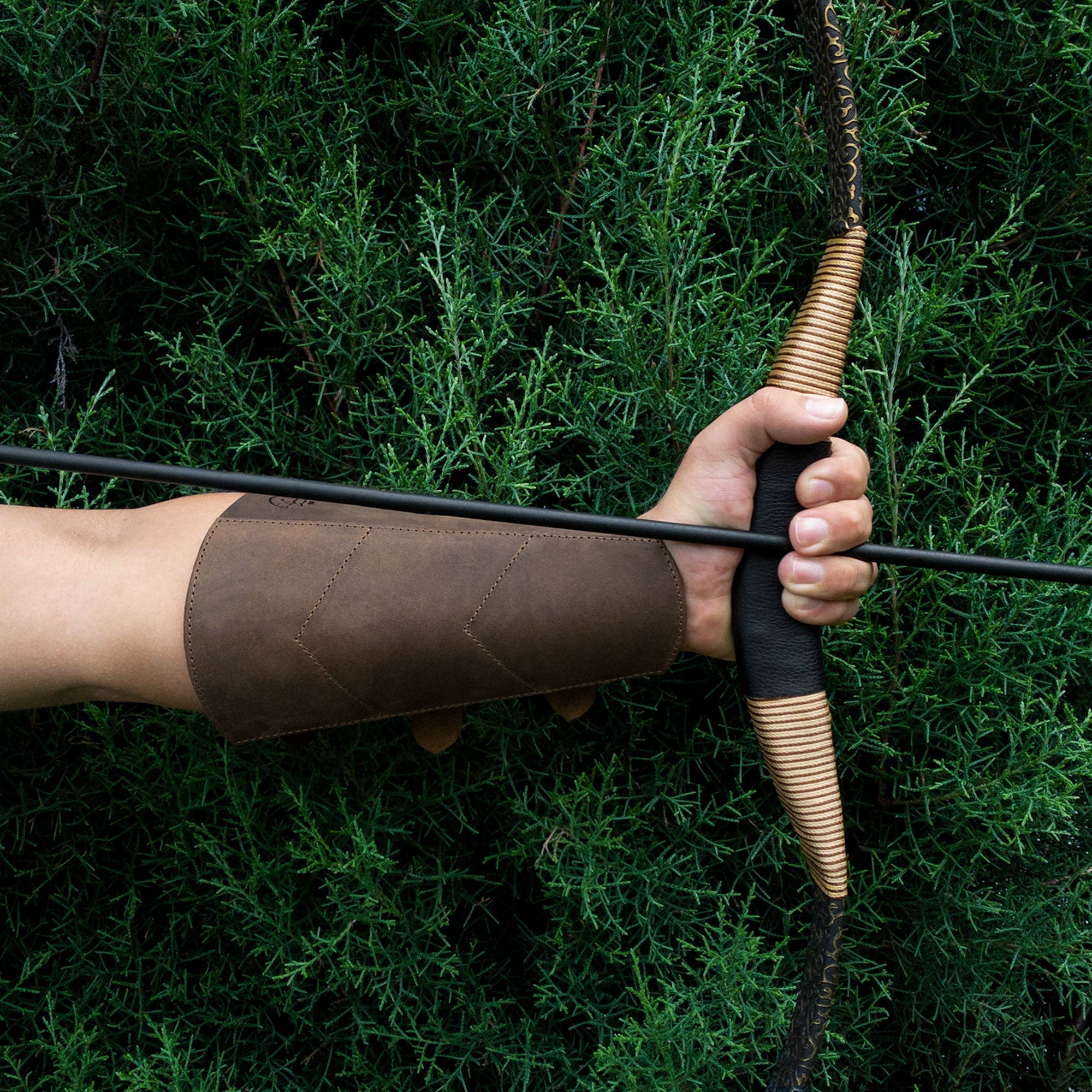 A hand gripping a bow with the Valhalla Gear Archery Forearm Protector for Bow Shooting Practice visible, demonstrating its function as an effective Arm Guard for training and cosplay. Crafted from durable Full Grain Leather, it showcases the artistry of StockyardX's Small Batch Production, Hand Cut, and Hand Sewn techniques, Fire Branded for authenticity. Handmade in La Antigua Guatemala & Oaxaca Mexico.