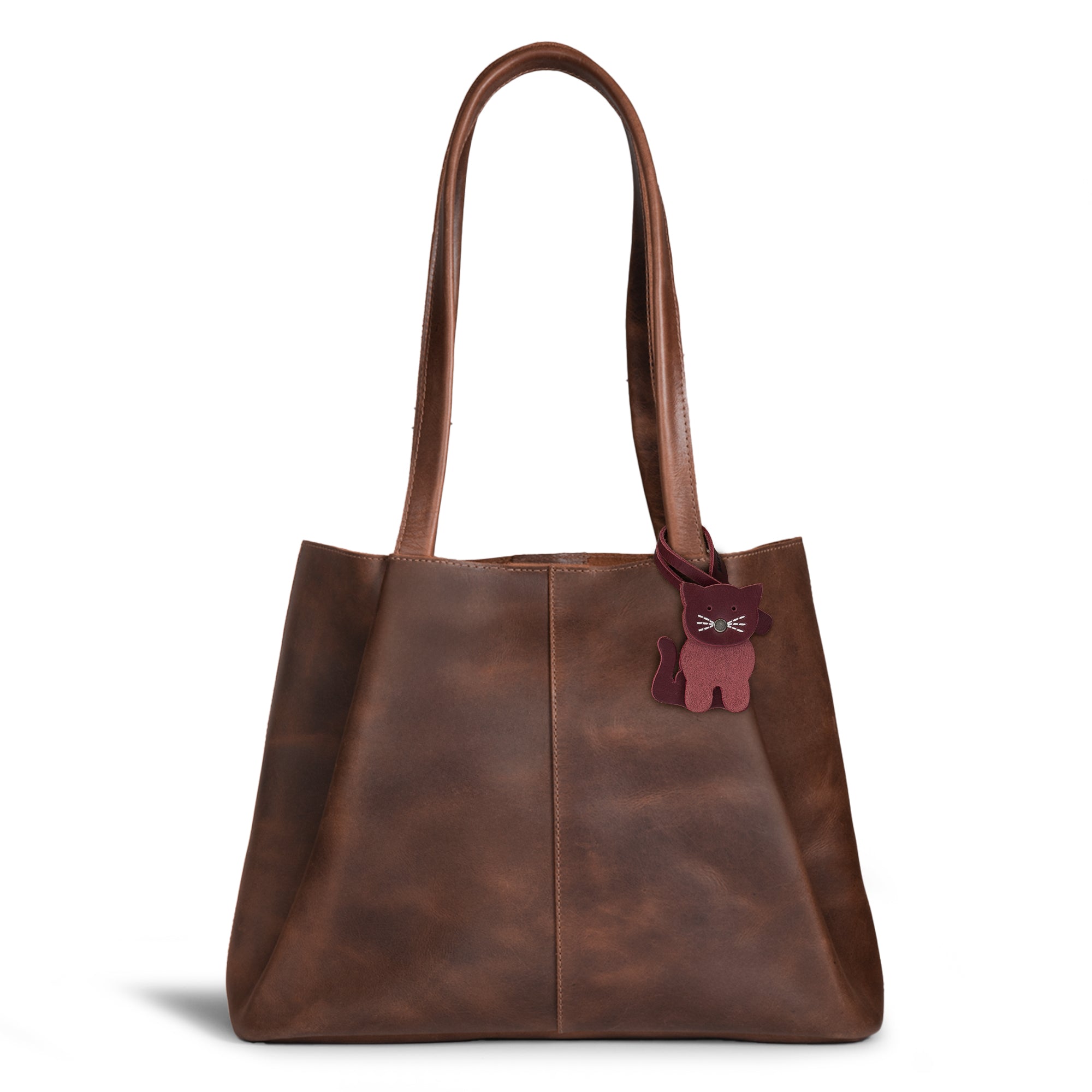 Hide & Drink Bag Charms attached to a stylish brown handbag, displaying a delightful cat design, perfect for personalizing. This purse charm for tote & backpacks is crafted using premium full grain leather. Each piece represents StockyardX's commitment to small batch production with hand cut, hand sewn details and fire branded artistry, handmade in La Antigua Guatemala & Oaxaca Mexico.