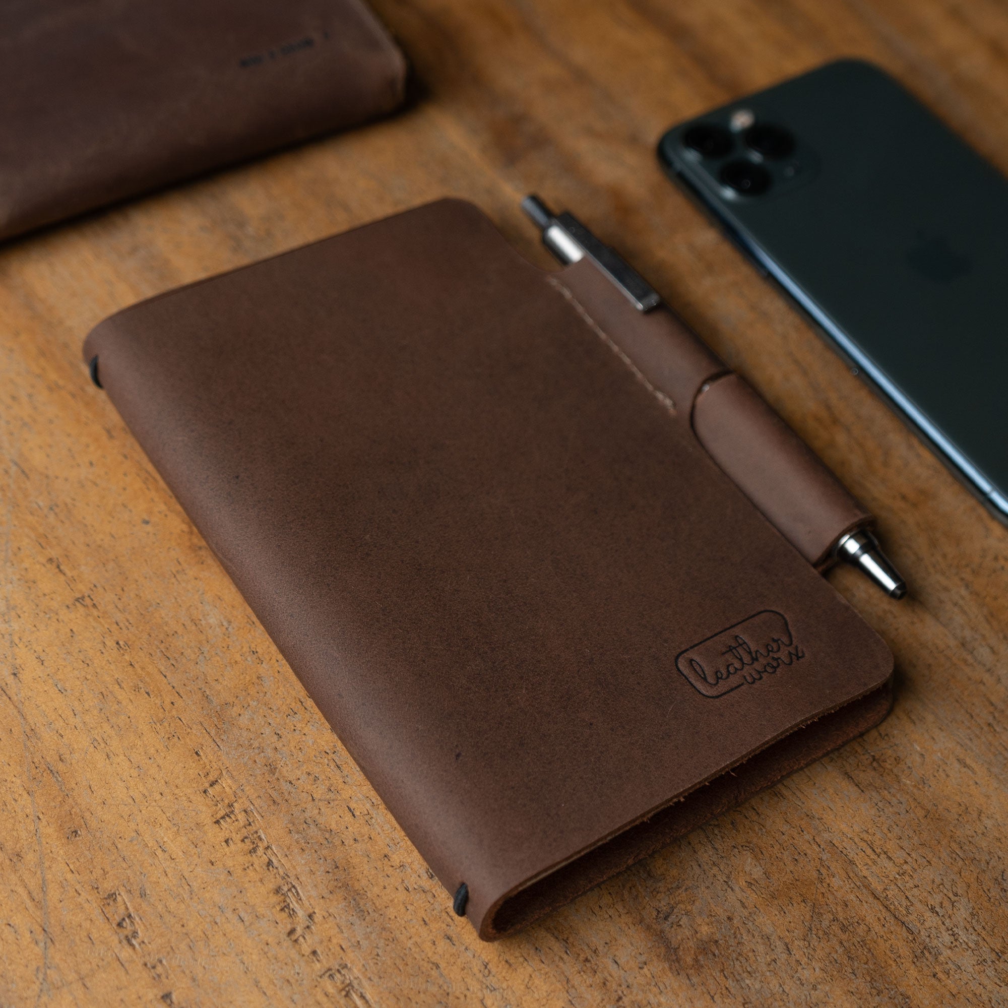 Artistic shot of the Vintage Cover for Field Notes (3.5 x 5.5 in. Notebook not Included) by Leather Worx, placed on a wooden surface. This Vintage Cover Designed for Field Notes Notebook (3.5 x 5.5 in.) reflects quality through small batch production, hand cut, hand sewn techniques, and a fire branded logo, handmade in La Antigua Guatemala & Oaxaca Mexico.