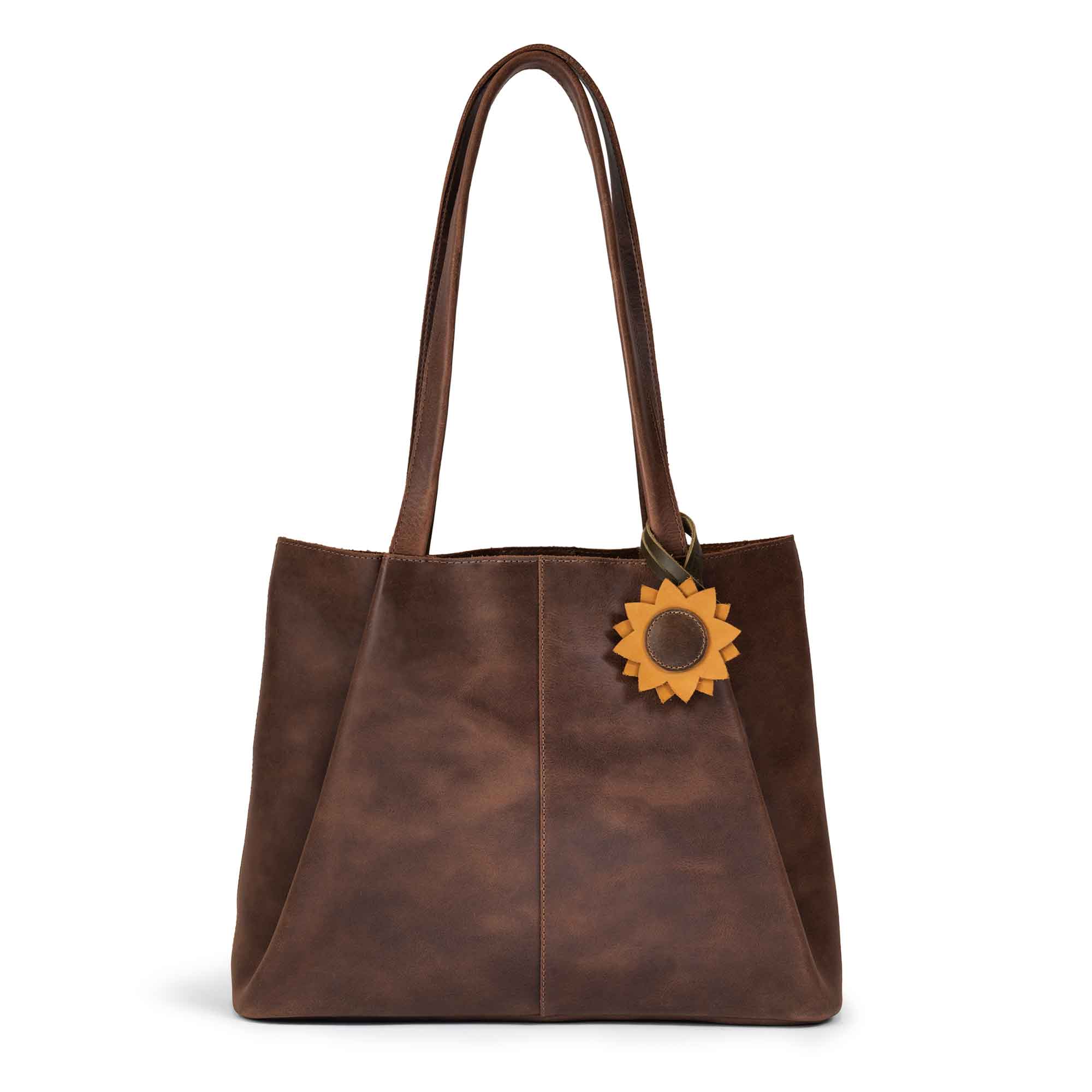 Hide & Drink Bag Charms attached to a stylish brown handbag, showcasing a sunflower charm perfect for accessorizing. This purse charm for tote & backpacks made from full grain leather represents StockyardX's dedication to small batch production. Each hand cut, hand sewn piece is fire branded, embodying artisan craftsmanship, handmade in La Antigua Guatemala & Oaxaca Mexico.