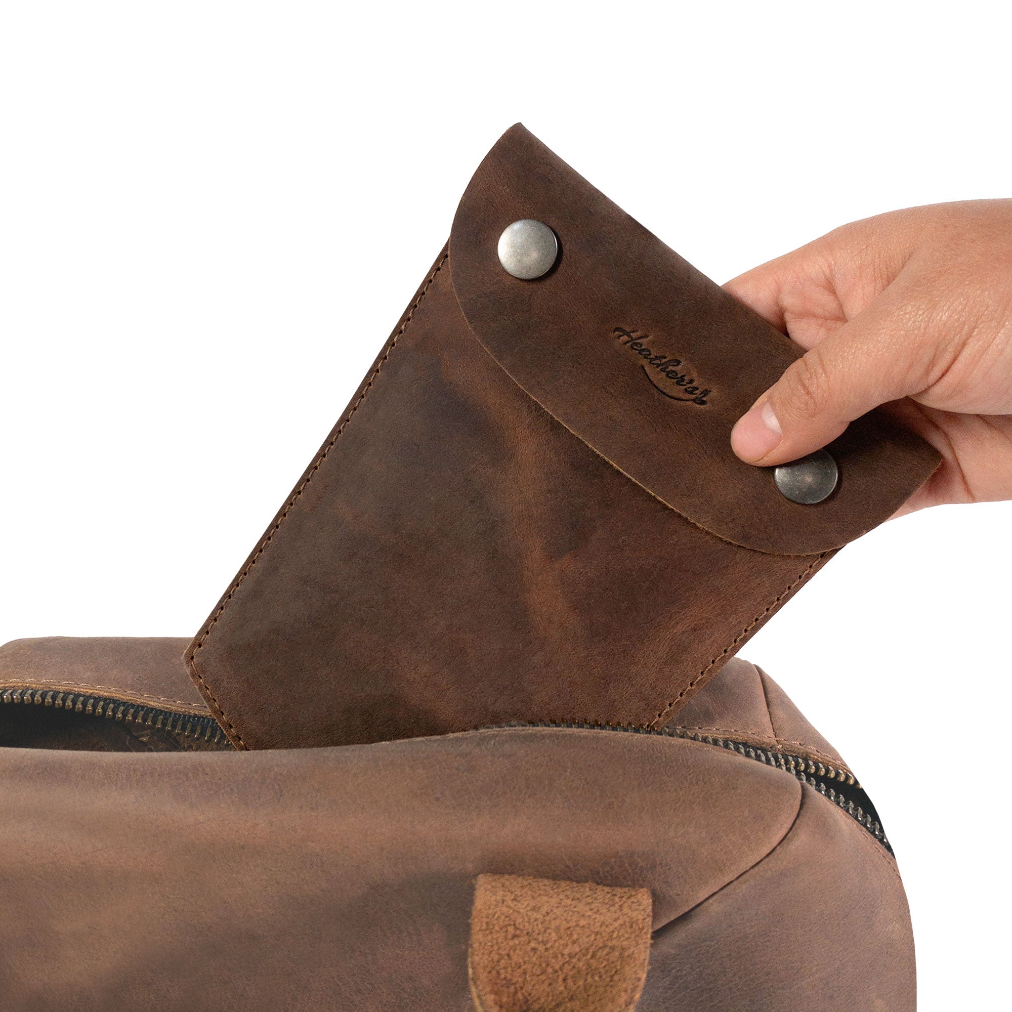 Heather's Essential Mini Bag being pulled from a backpack, demonstrating its convenient size and functionality. This mini bag for women is an essential case for glasses, makeup, USB, cables and cash, ideal for travel. Crafted from full grain leather in La Antigua Guatemala, it's made through small batch production, hand cut, hand sewn, and fire branded by skilled artisans.