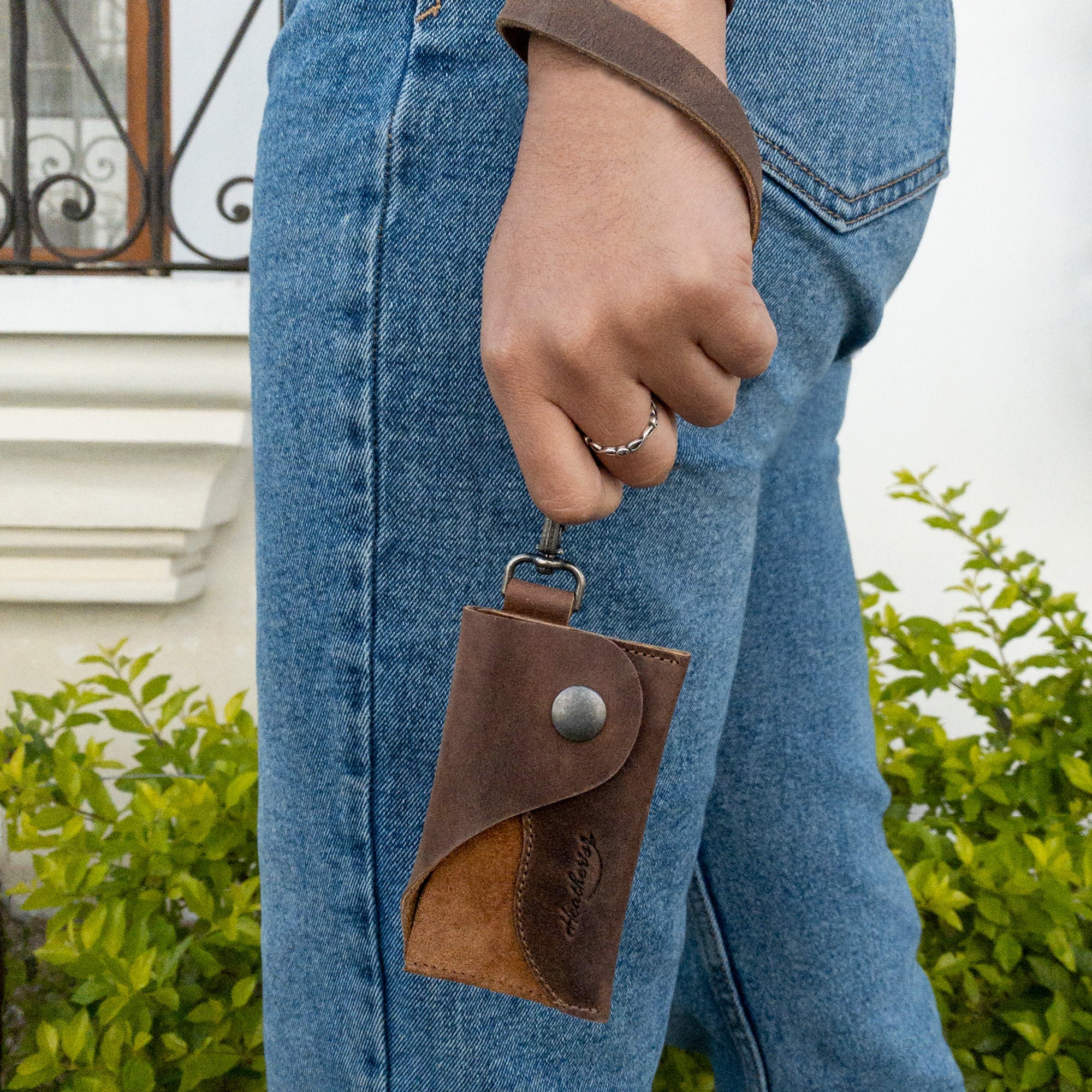 A person holding Heather's Female Wallet with Wristlet, highlighting its unique ID case with wrist strap made of full grain leather. This wallet serves as a perfect money holder and travel organizer, crafted through small batch production by artisans in La Antigua Guatemala and Oaxaca Mexico.