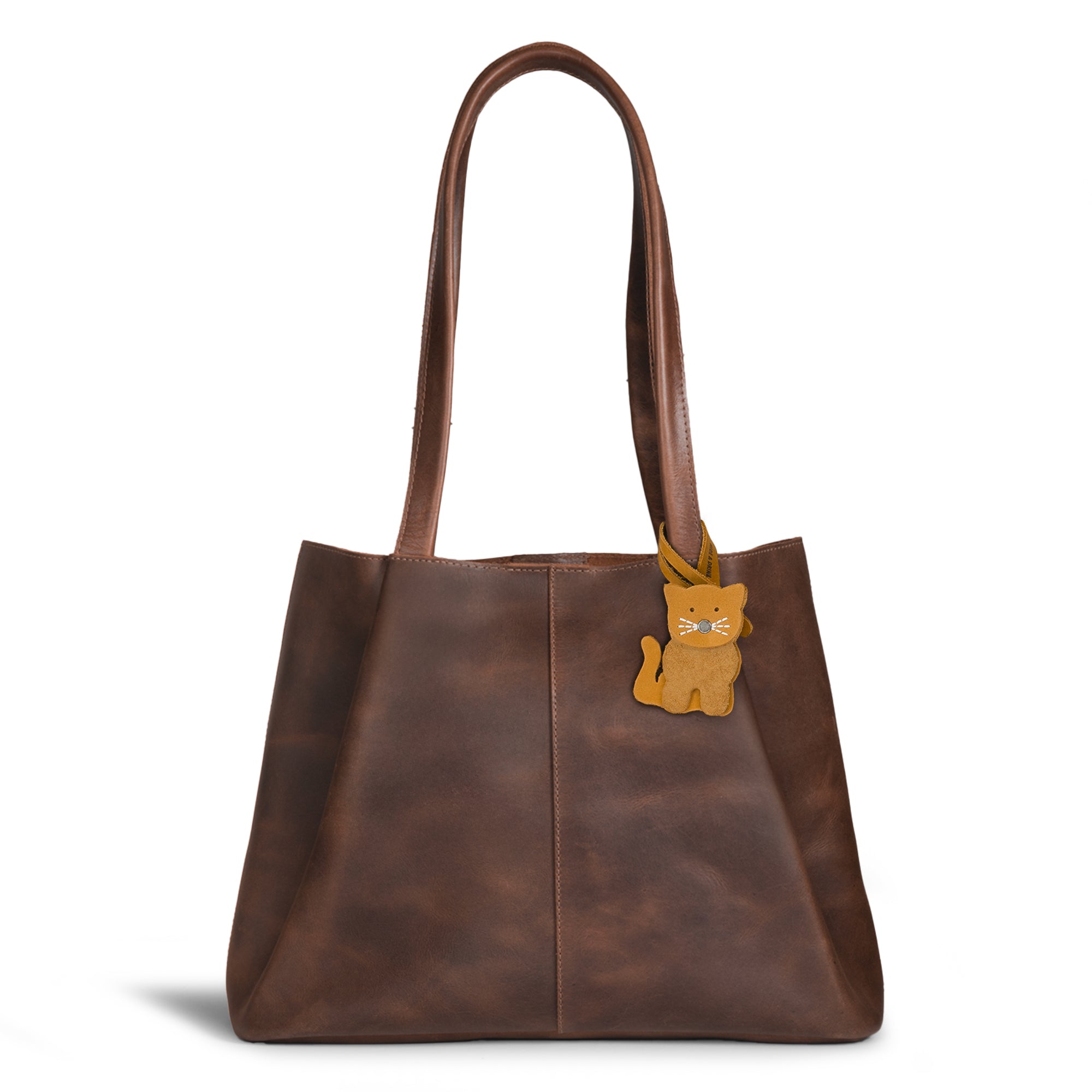 Hide & Drink Bag Charms displaying a charming cat design attached to a trendy brown handbag. This purse charm for tote & backpacks is made from durable full grain leather, representing StockyardX's focus on small batch production. Each piece features meticulous hand cut, hand sewn details and fire branding, handmade in La Antigua Guatemala & Oaxaca Mexico.