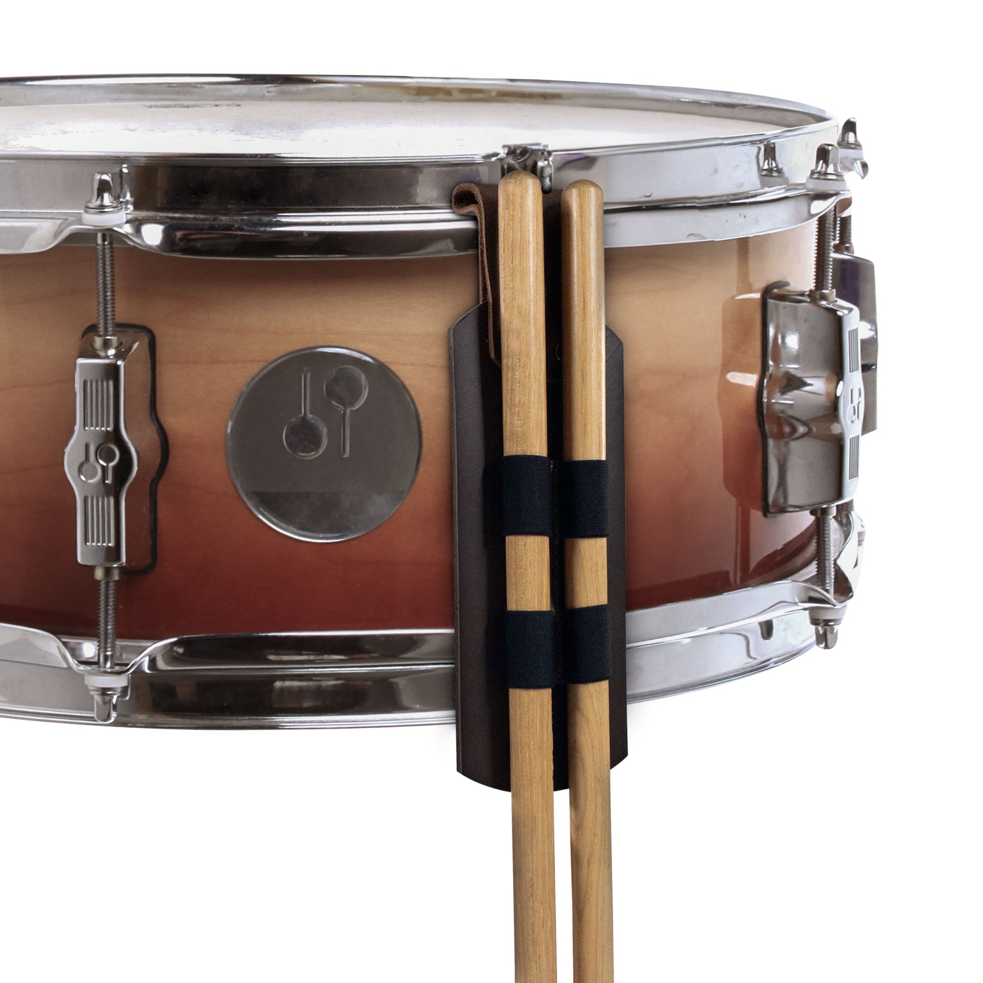A close-up of a snare drum featuring the Set of 2 Drum Stick Sleeves by tocame. This image highlights the rustic hanging sleeve securely holding two drumsticks, made from durable full grain leather and crafted in small batch production by artisans in La Antigua, Guatemala.