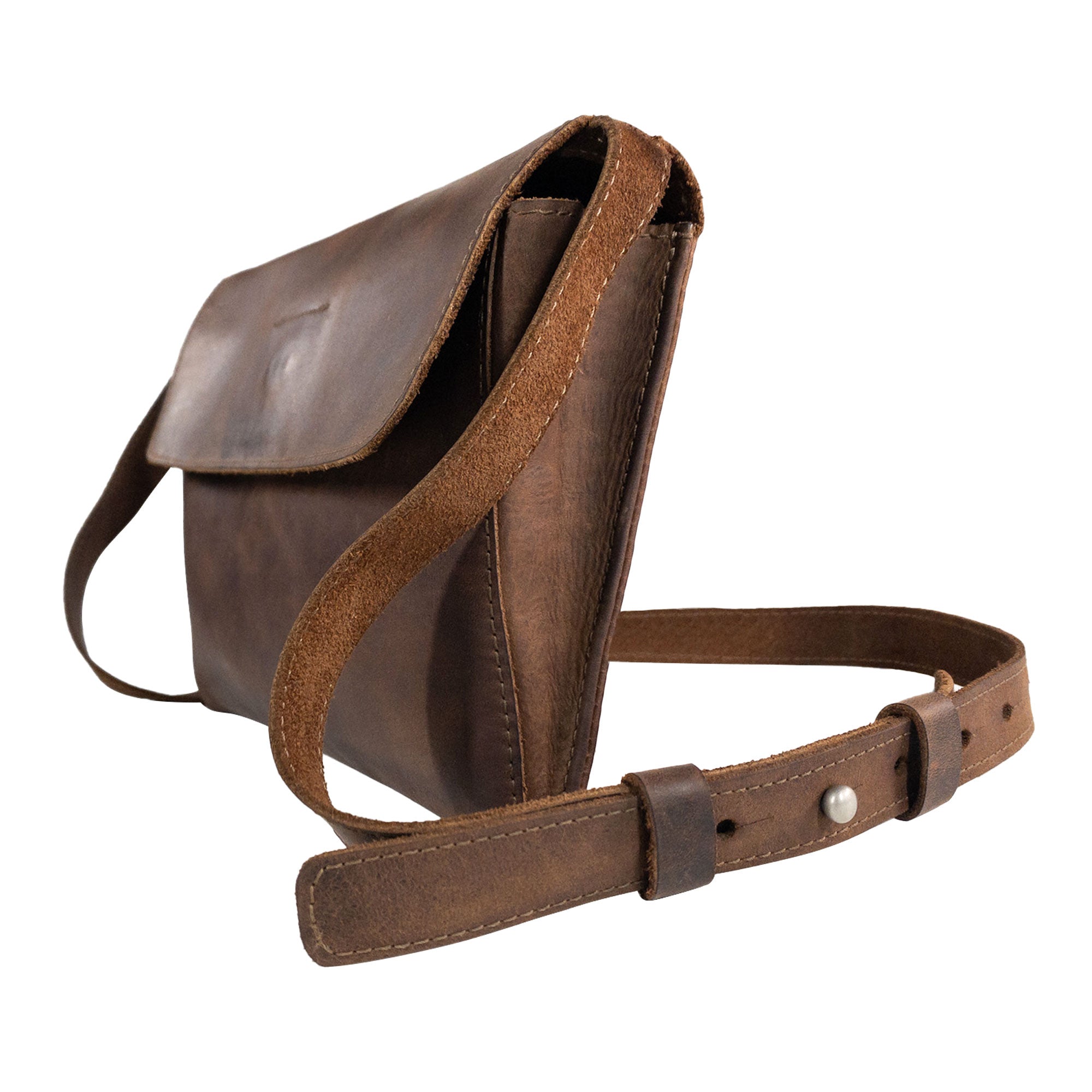 A side view of the Minimalist Shoulder Bag by Hide & Drink highlights its clean design and full grain leather construction. This rectangular messenger bag with an adjustable strap is a versatile travel accessory. Enjoy the unique, handmade quality of this Mini Classic Shoulder Bag, a testament to artisan craftsmanship from La Antigua Guatemala & Oaxaca Mexico.