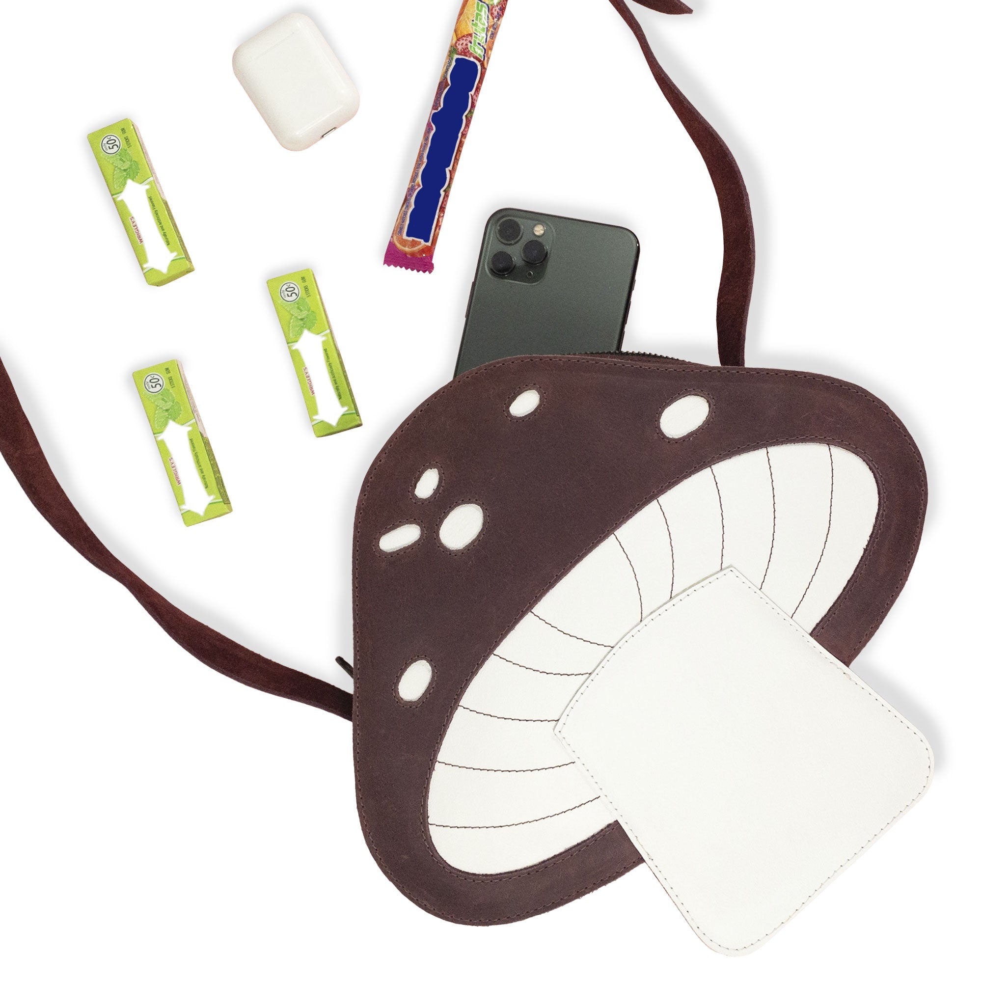 The Mushroom-Shaped Leather Shoulder Bag by Tudi Frudi is shown here filled with everyday items, demonstrating its practicality as a crossbody bag. This playful bag, made from Full Grain Leather, serves well as a travel or messenger bag, reflecting the quality of small batch production with artisan craftsmanship from La Antigua Guatemala.