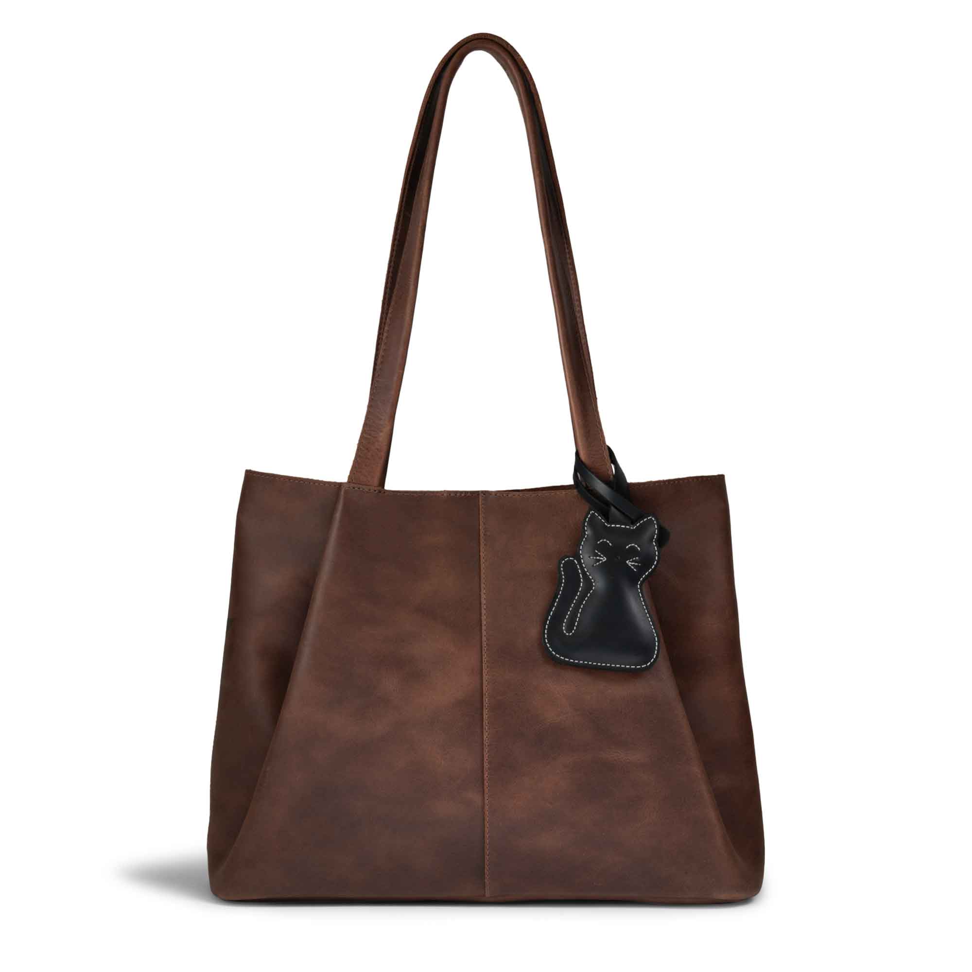 Hide & Drink Bag Charms attached to a stylish brown handbag, showcasing a golden cat design perfect for personalization. This purse charm for tote & backpacks is made from high-quality full grain leather, representing StockyardX's focus on small batch production with hand cut, hand sewn details and fire branding, handmade in La Antigua Guatemala & Oaxaca Mexico.