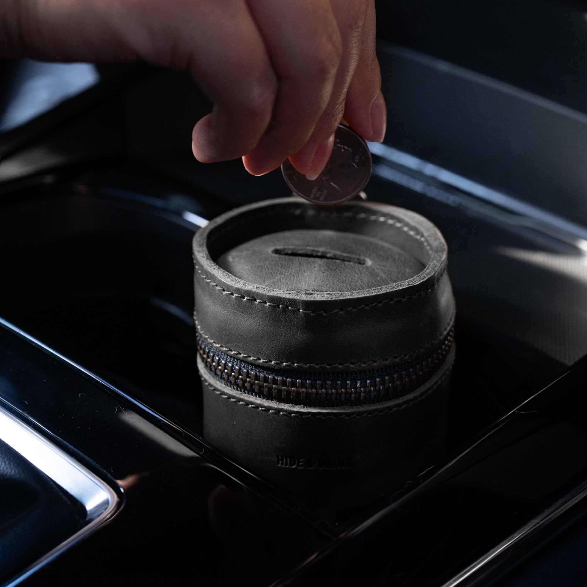 User dropping a coin into Hide & Drink's black Bucket Coin Release pouch, illustrating its practicality. This full grain leather coin purse for men and women is a beautifully crafted money saving box, made through artisan techniques.