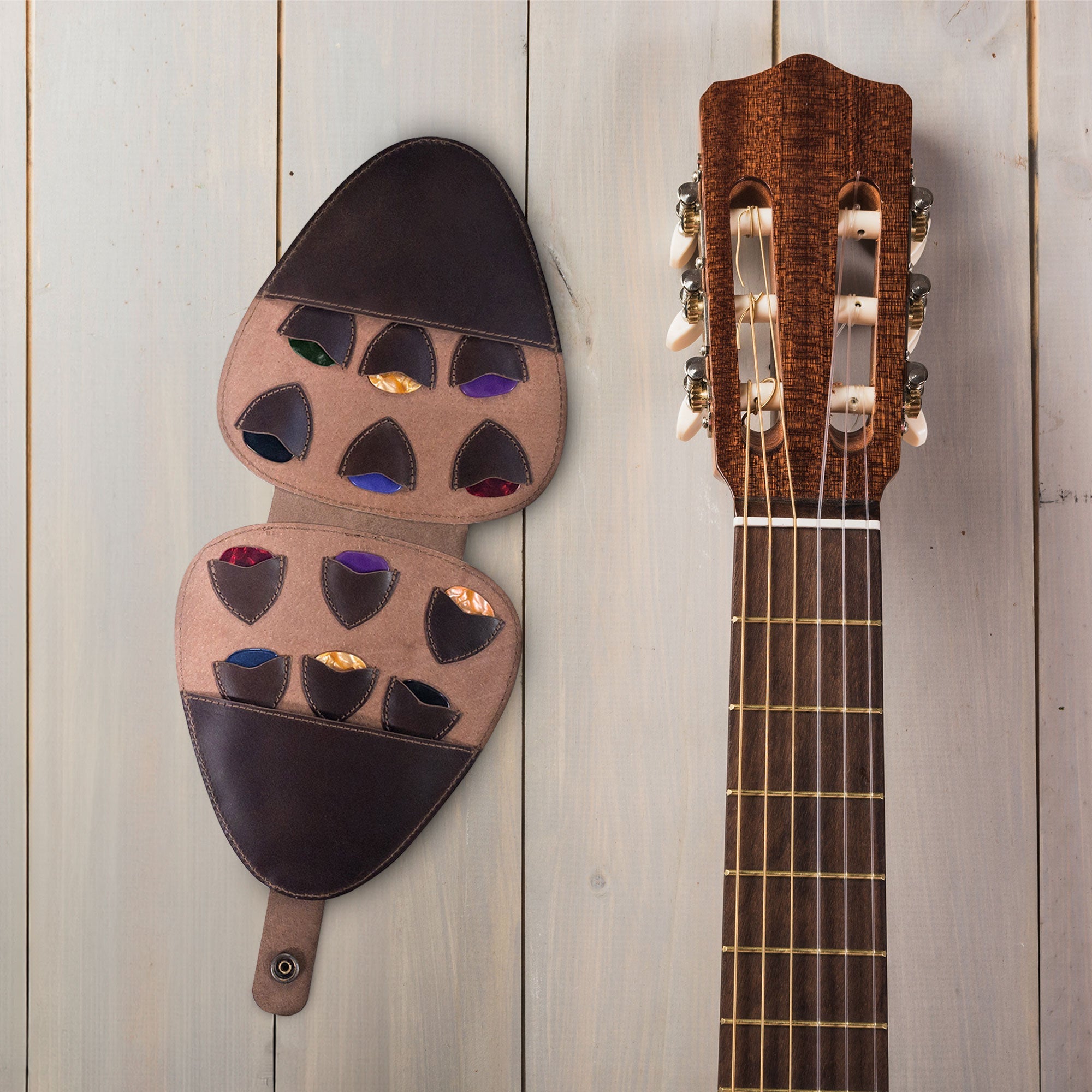 Guitar Pick Case (Guitar Picks Not Included) by tocame displayed next to a guitar, showcasing the Guitar Pick Case with 12 Slots. This Full Grain Leather Guitar Pick Holder is designed for musicians and features small batch production, hand cut, hand sewn craftsmanship, and is fire branded, handcrafted in La Antigua Guatemala & Oaxaca Mexico.