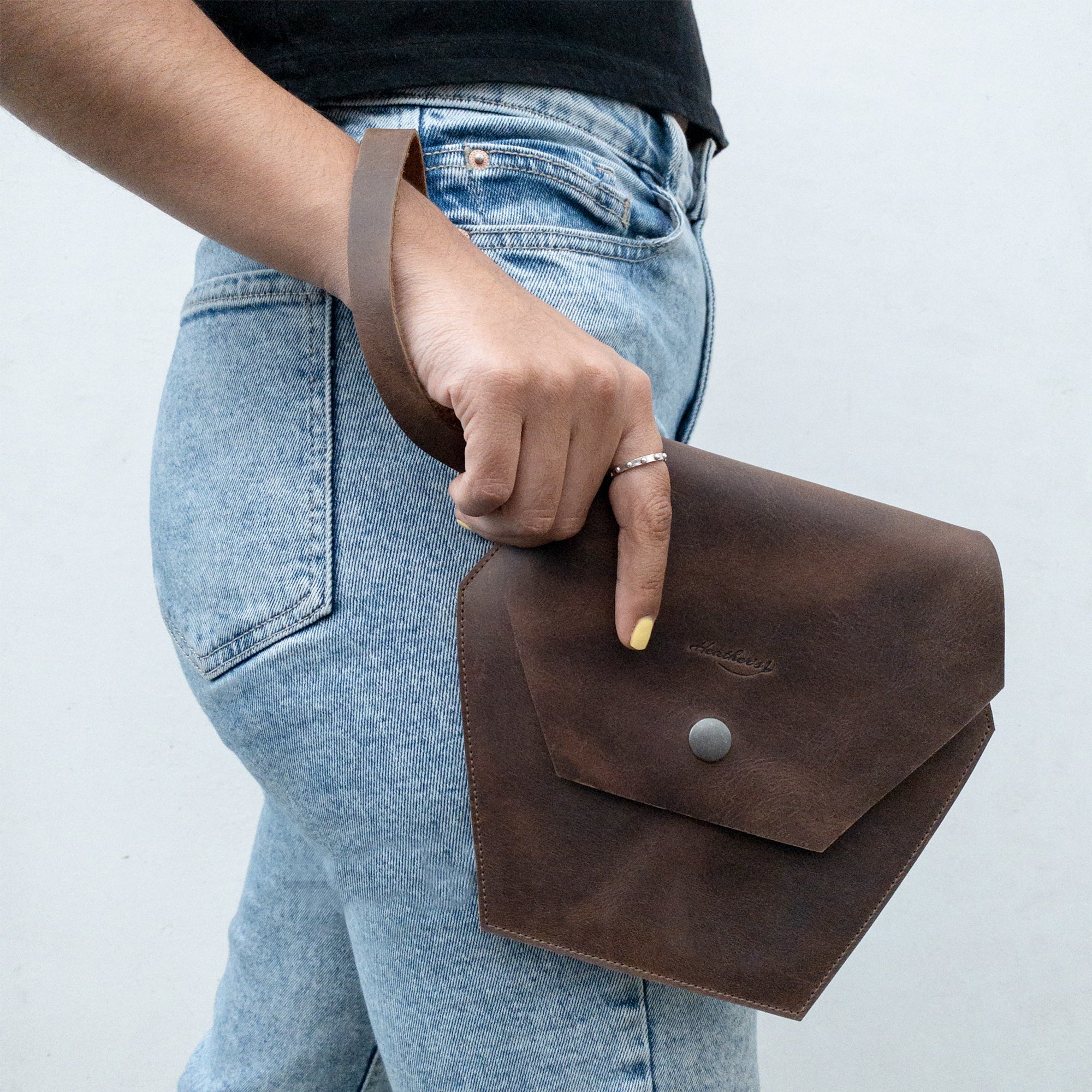 Woman holding Heather's Hexagonal Clutch Bag with wristlet, showcasing a stylish accessory for on-the-go moments. Made from Full Grain Leather, this clutch bag serves as a chic travel handbag for makeup and toiletry items, featuring artisan craftsmanship from La Antigua Guatemala & Oaxaca Mexico.