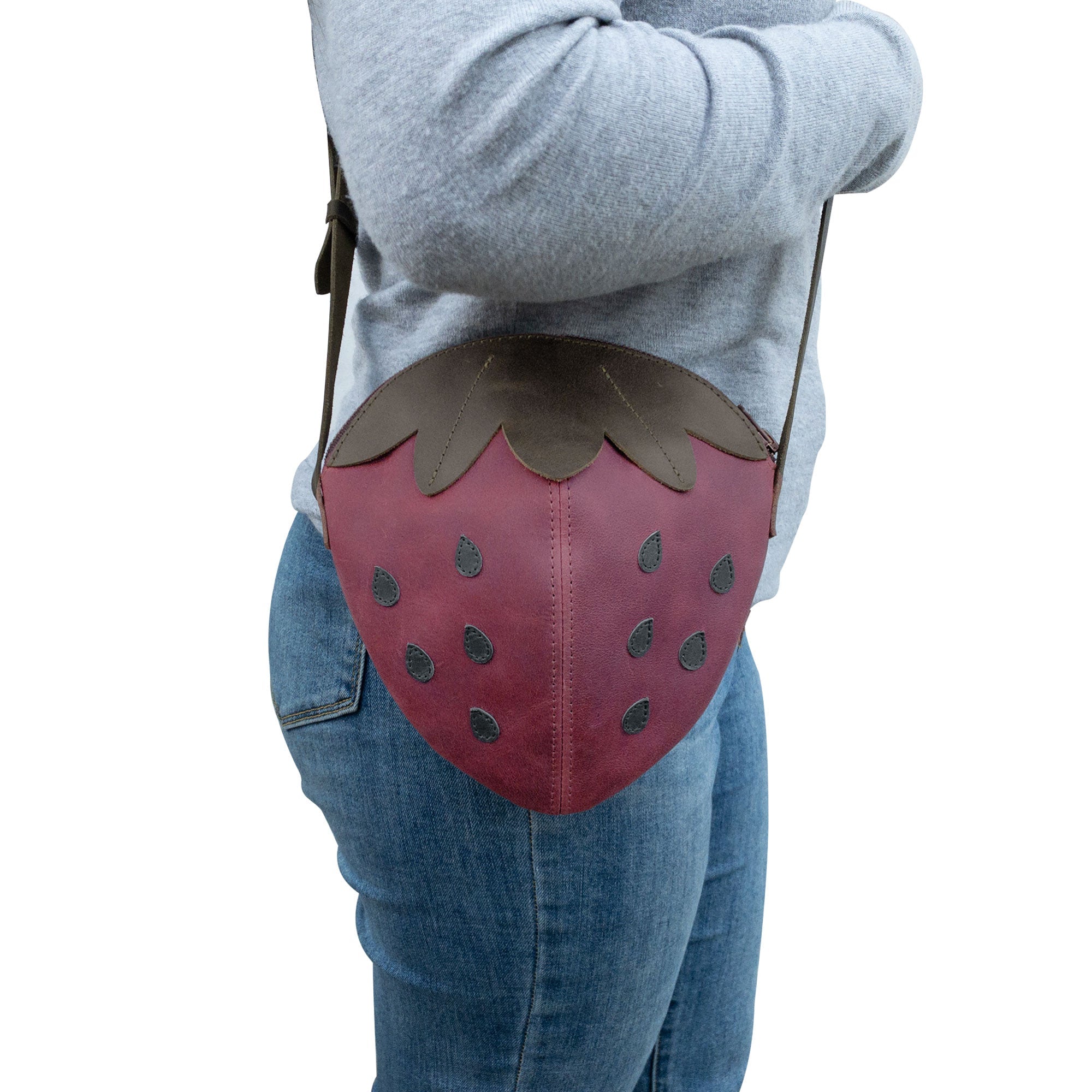 A model carrying the Leather Strawberry-Shaped Shoulder Bag by Tudi Frudi, demonstrating its stylish versatility. Made from Full Grain Leather, this crossbody bag is a must-have accessory, reflecting the quality of artisan craftsmanship from La Antigua Guatemala & Oaxaca Mexico, ensuring unique small batch production.
