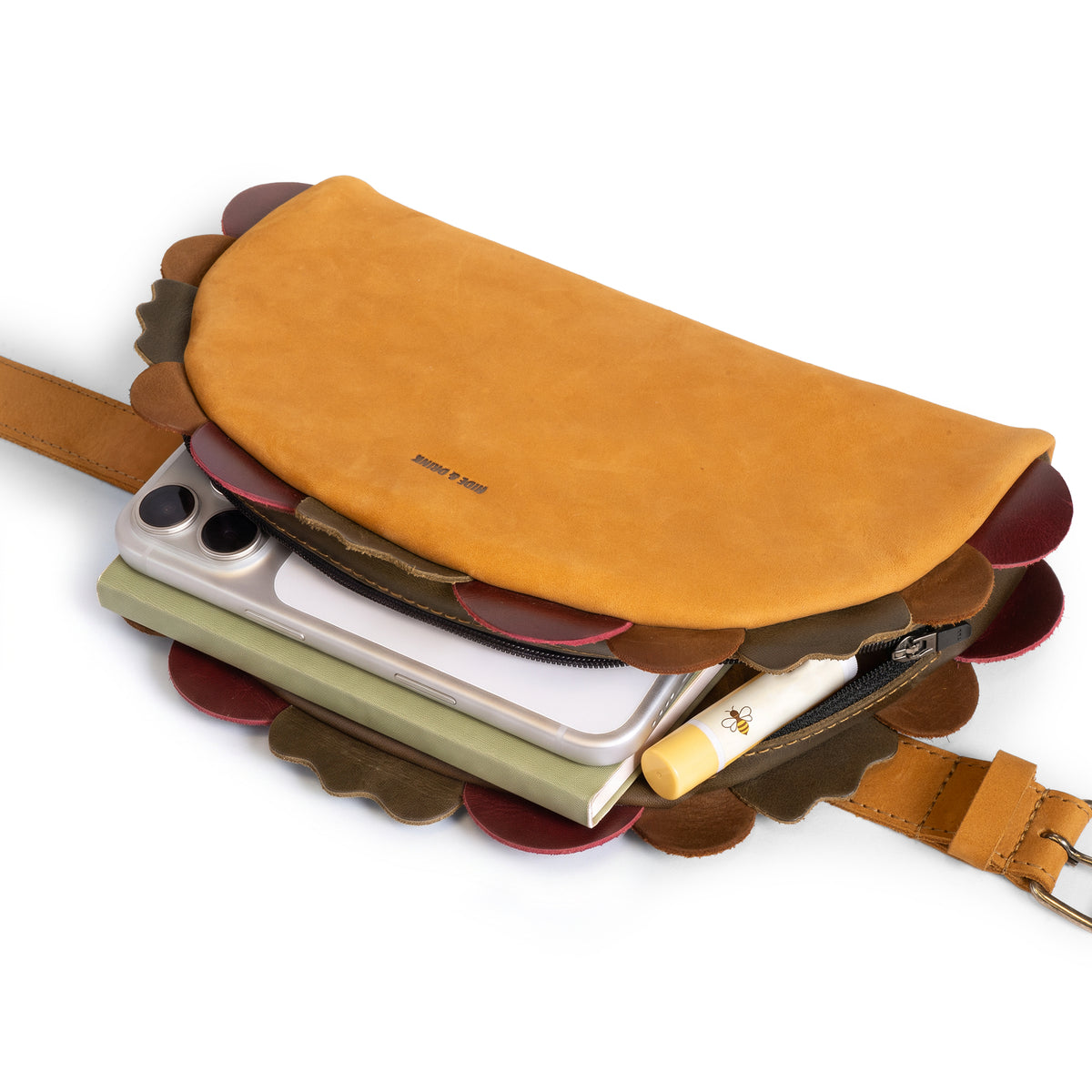 Hide & Drink Taco Fanny Pack opened to display a phone, notebook, pen, and everyday essentials inside the tan full grain leather waist bag. This fun belt bags style is a zippered bags travel carrier, outdoor waist pouch, carry on case, and practical travel accessory from StockyardX, made through small batch production with hand cut, hand sewn, fire branded artisan craftsmanship, handmade in La Antigua Guatemala & Oaxaca Mexico.