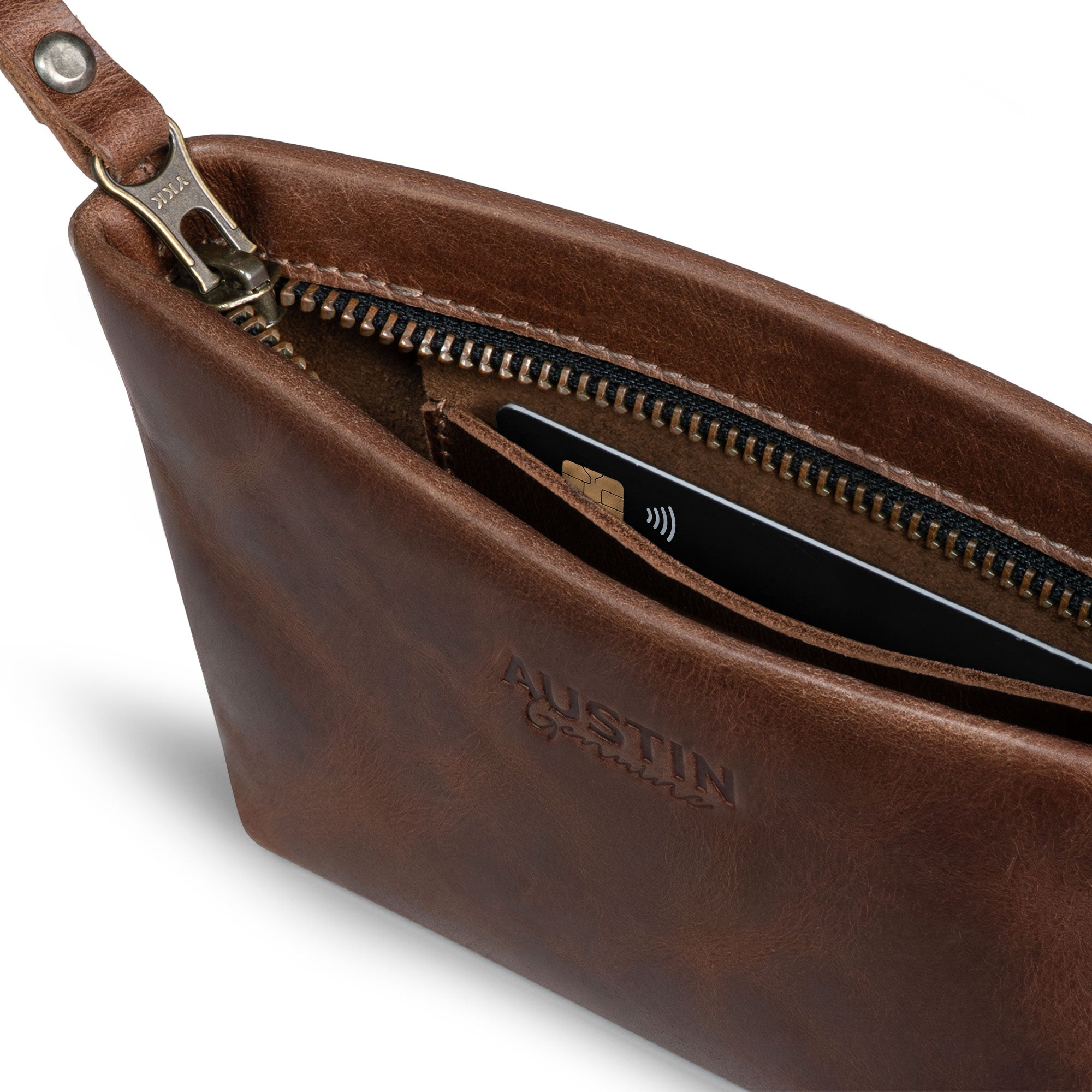 Close-up of the Austin Genuine The Seaholm Makeup Bag showing its brass zipper, leather wrist strap, card slot, and brown Full Grain Leather finish; StockyardX Small Batch Production, Hand Cut, Hand Sewn, Fire Branded, Artisan, Handmade in La Antigua Guatemala & Oaxaca Mexico.