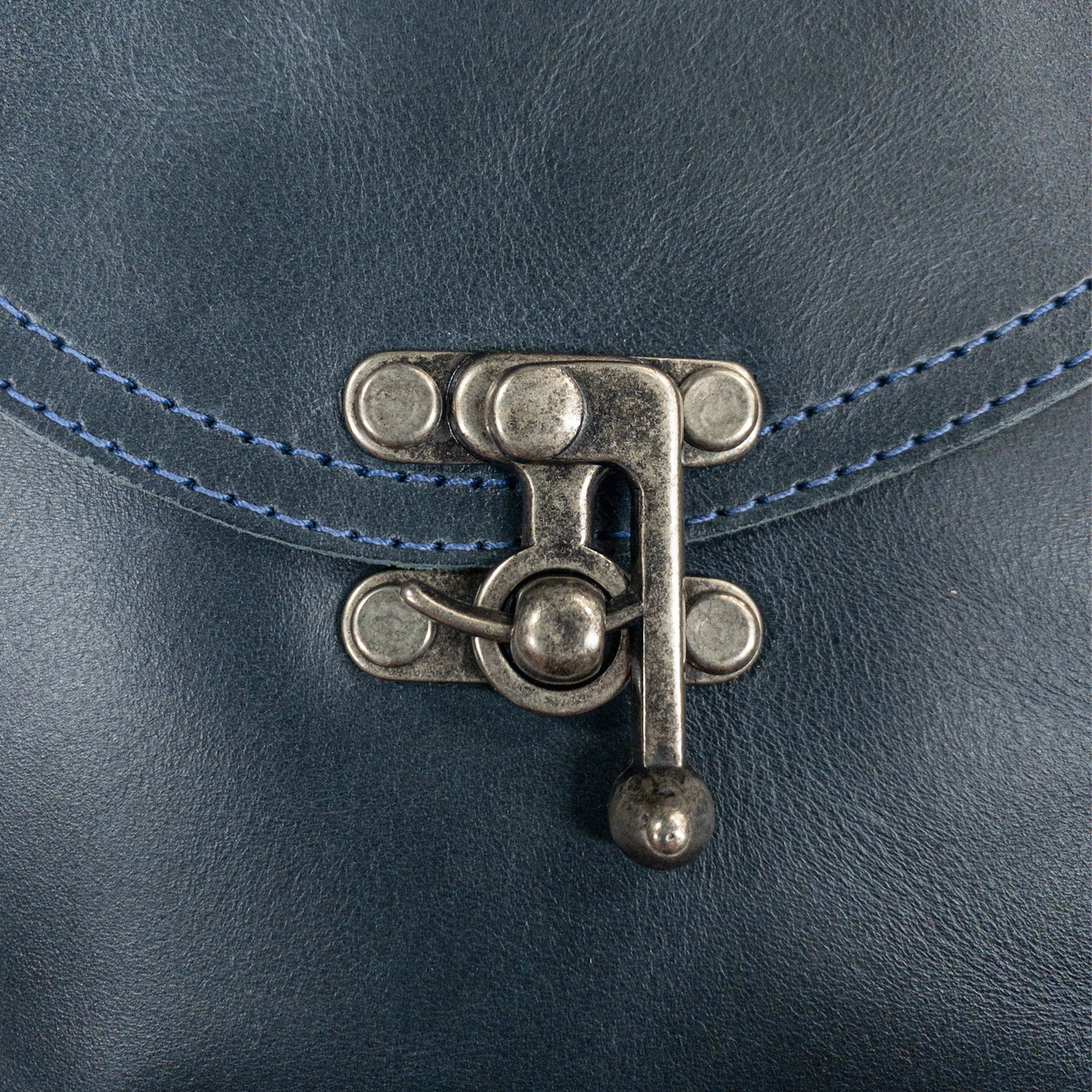 Close-up of the vintage clasp on the navy Petite Vintage Clutch Bag by Hide & Drink, focusing on the fine details. This elegant handbag made from full grain leather is perfect as an evening bag or travel accessory, representing artisan quality from La Antigua Guatemala & Oaxaca Mexico.