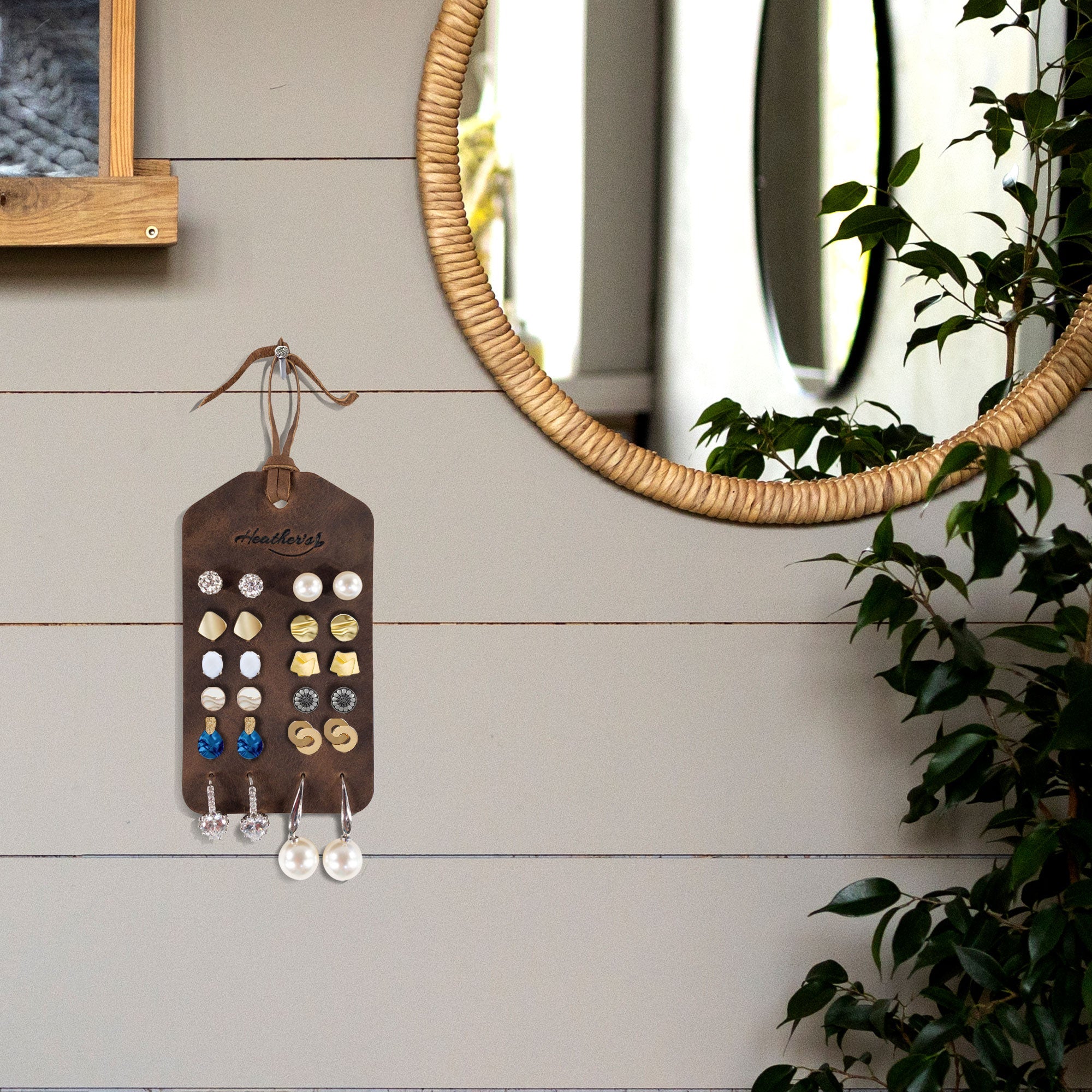 A stylish display of the Set of 2 Earring Tags by Heather's hung on a wall, showcasing various earrings. These full grain leather tags with pre-cut holes are a must-have travel accessory, handmade in La Antigua Guatemala & Oaxaca Mexico, reflecting artisan craftsmanship with hand cut and hand sewn detail.