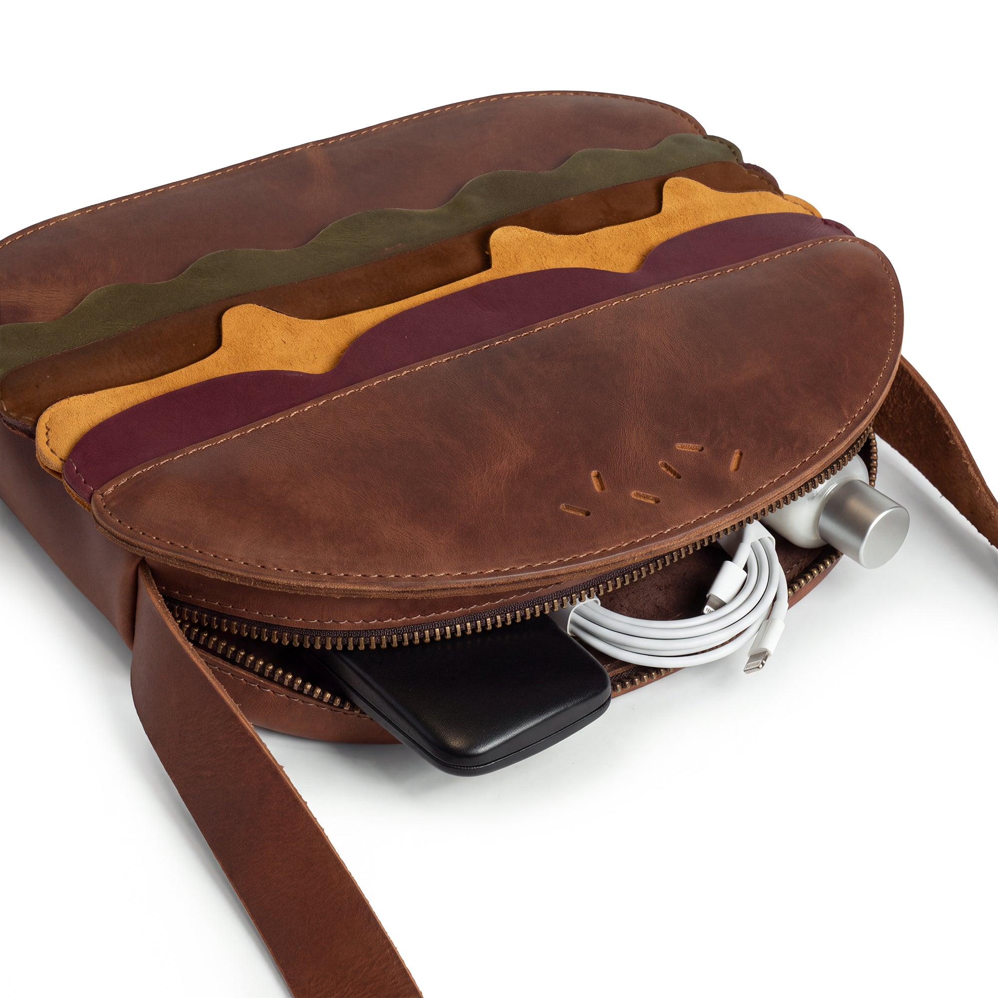 Open Burger-Shaped Shoulder Bag by Tudi Frudi, showcasing its ample storage with included items. This artisanal bag made from Full Grain Leather serves as a fantastic Crossbody Bag and Messenger Bag, adding a playful element to your travel accessories. Carefully crafted in small batches, it's handmade in La Antigua Guatemala & Oaxaca Mexico, perfect for everyday use.