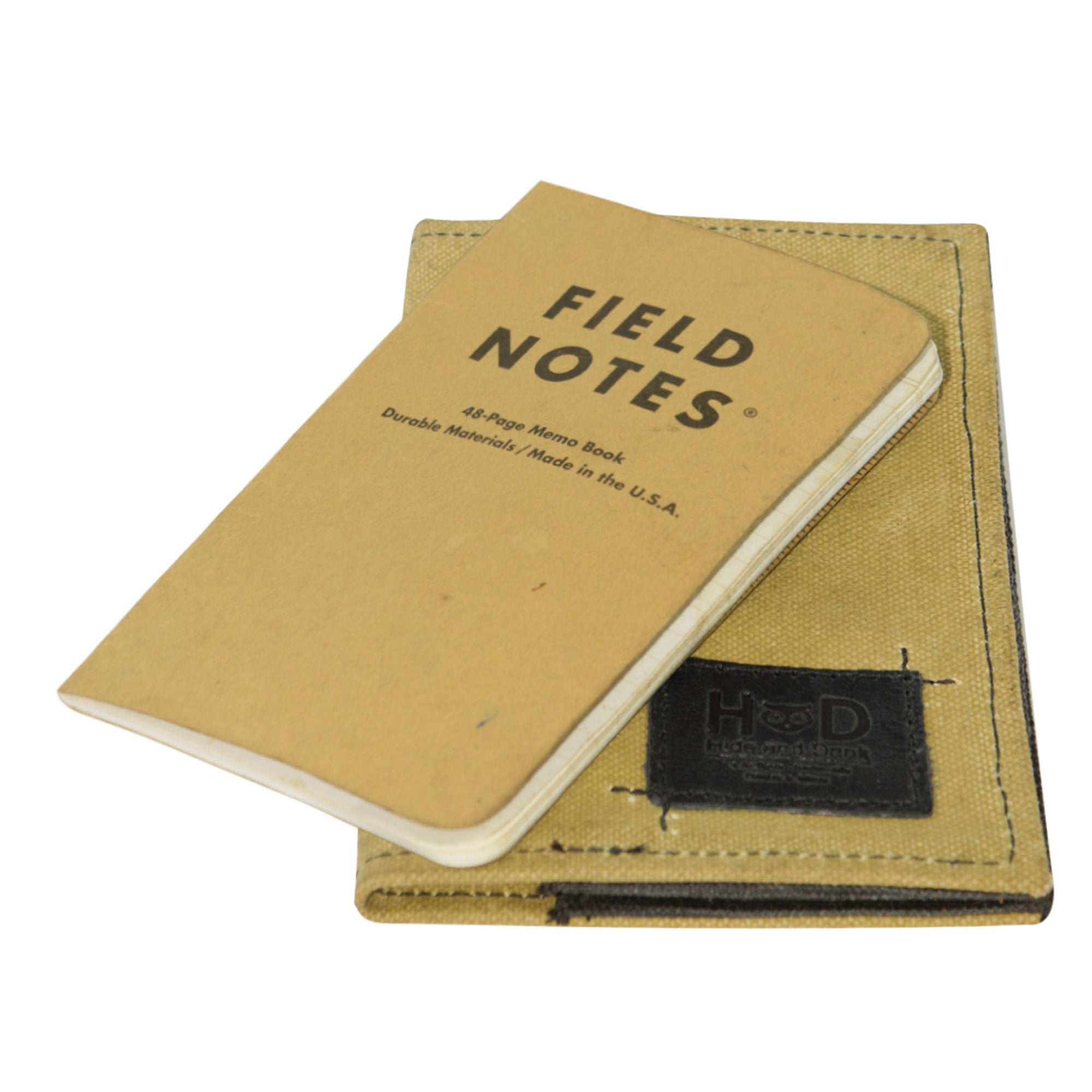Hide & Drink Waxed Canvas Field Notes Cover paired with other creative journaling materials, emphasizing its versatile use. This journal cover, designed for travelers, has ample space and compartments, crafted with a focus on quality and function.