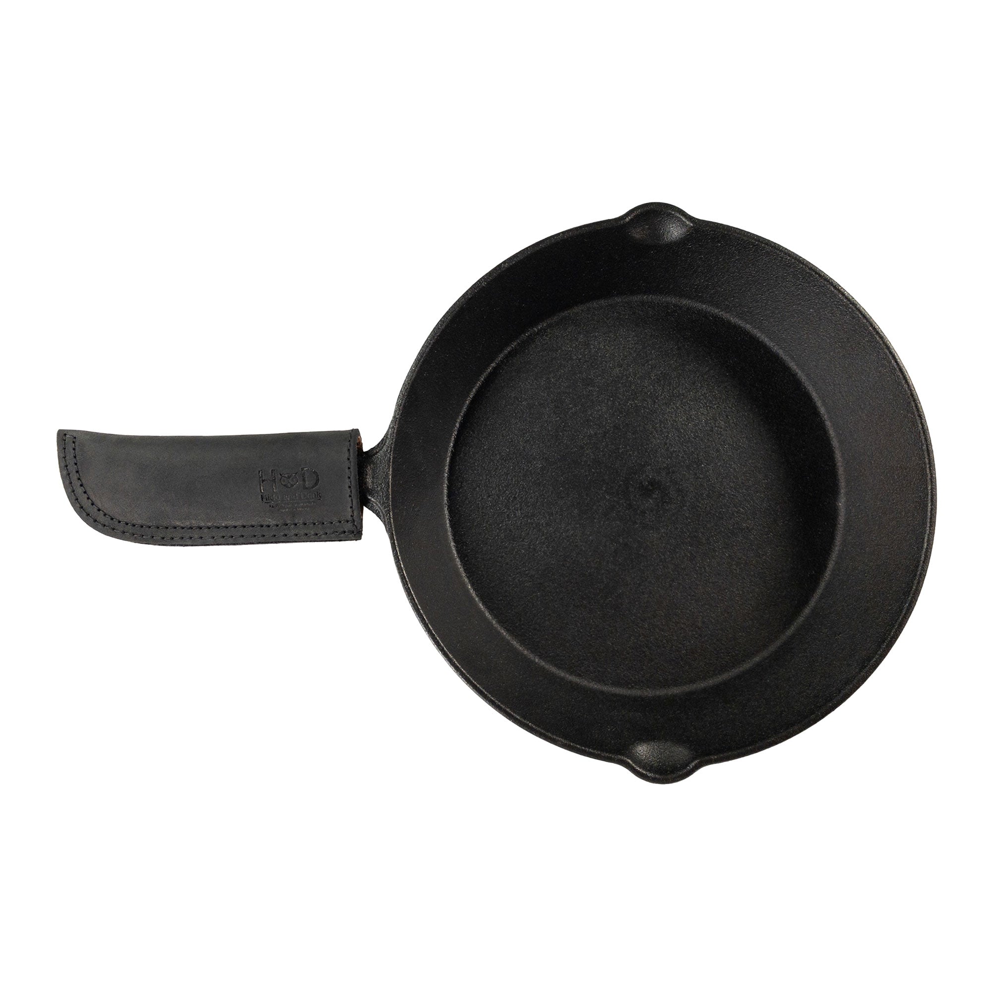 Hide & Drink Cast Iron Panhandle Cover prominently displayed on cookware, showcasing its practical design. This artisan hot handle protector is crafted from double stitched full grain leather, designed to slide easily onto metal skillets for cooking safety. Handmade in La Antigua Guatemala & Oaxaca Mexico, it adds comfort and style.
