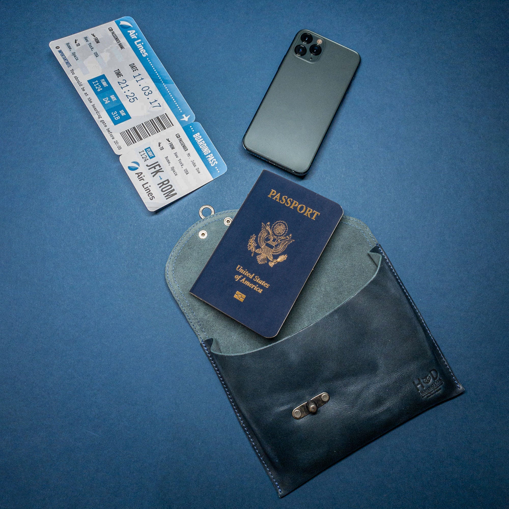 The navy Petite Vintage Clutch Bag by Hide & Drink displayed with travel essentials, showcasing its versatility. This chic evening bag made from full grain leather is perfect for travel, highlighting quality artisan craftsmanship from small batch production in La Antigua Guatemala & Oaxaca Mexico.