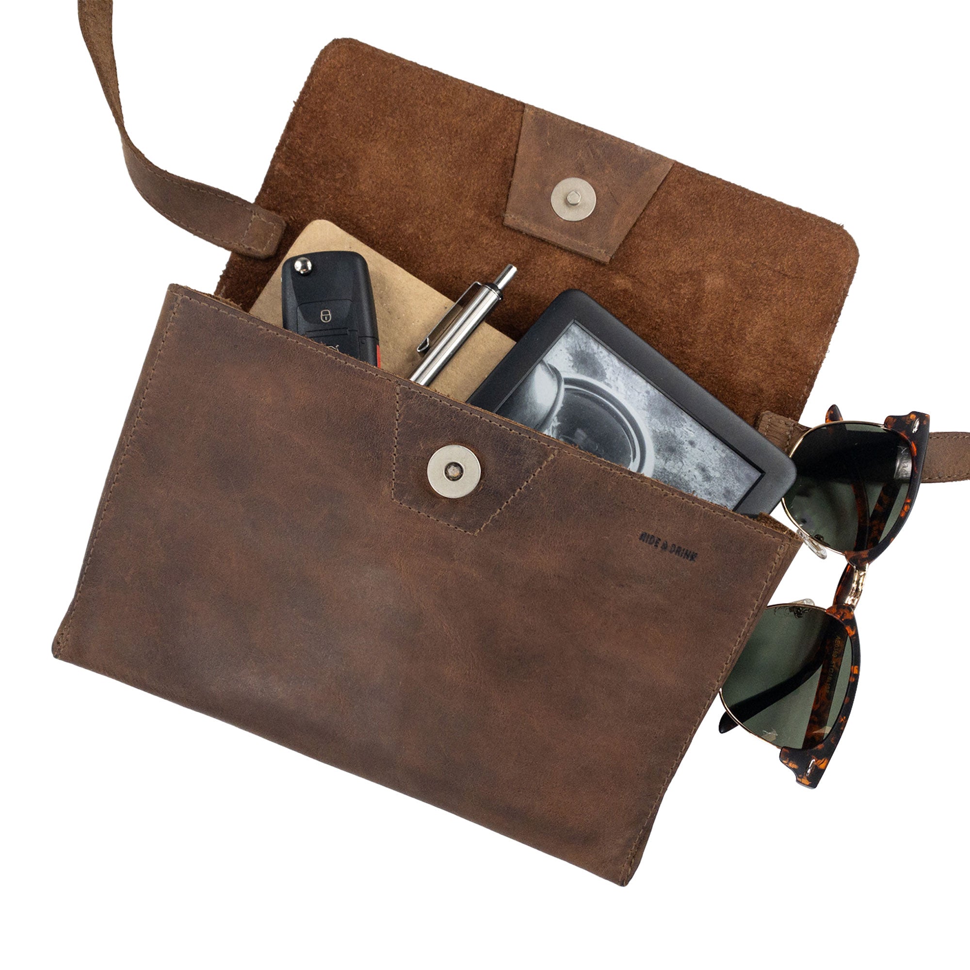 The Minimalist Shoulder Bag by Hide & Drink with items inside shows its spacious design, ideal for everyday use. This rectangular messenger bag is crafted from premium full grain leather, making it not just a stylish accessory but a functional travel companion. Experience the artisan touch of this Mini Classic Shoulder Bag, which is hand cut, hand sewn, and fire branded in La Antigua Guatemala & Oaxaca Mexico.