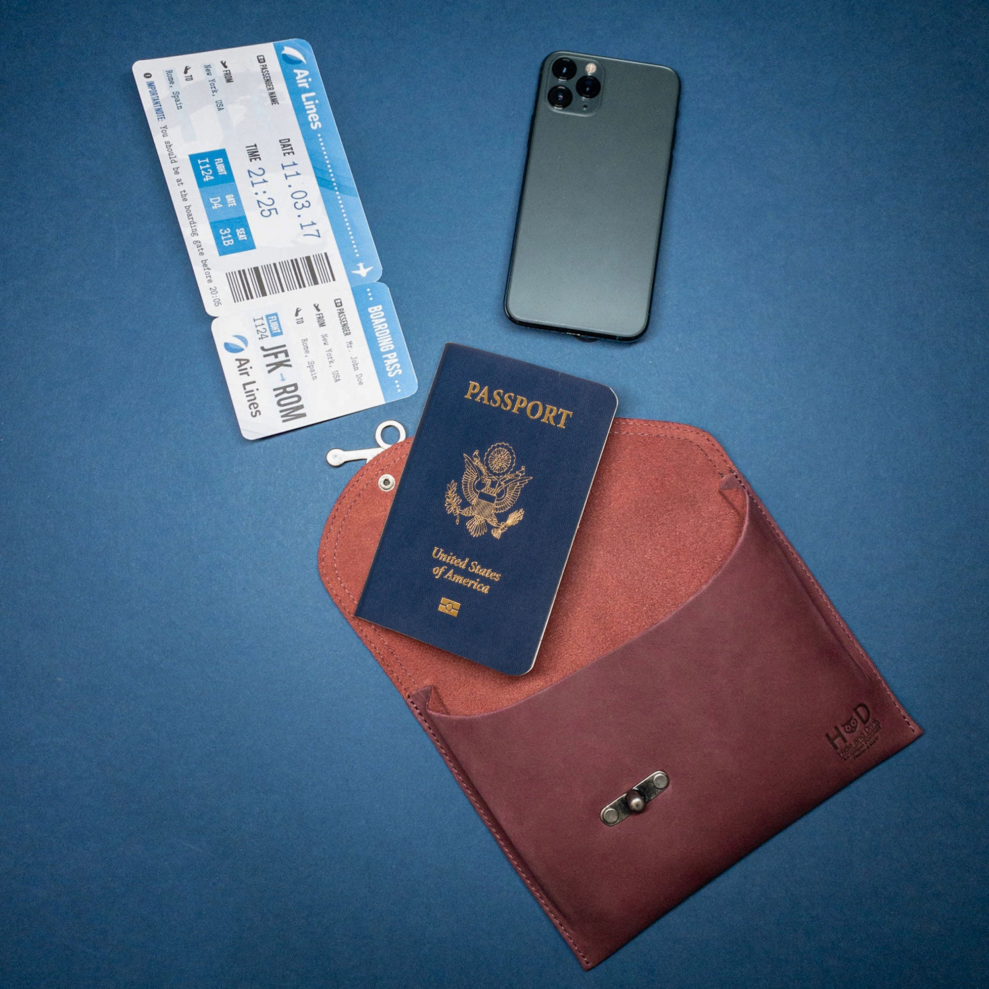 The Petite Vintage Clutch Bag by Hide & Drink displayed with travel essentials like tickets and a phone. This chic clutch serves as a functional evening bag and travel accessory, crafted from luxurious full grain leather, emphasizing its handmade artisan quality from La Antigua Guatemala & Oaxaca Mexico.