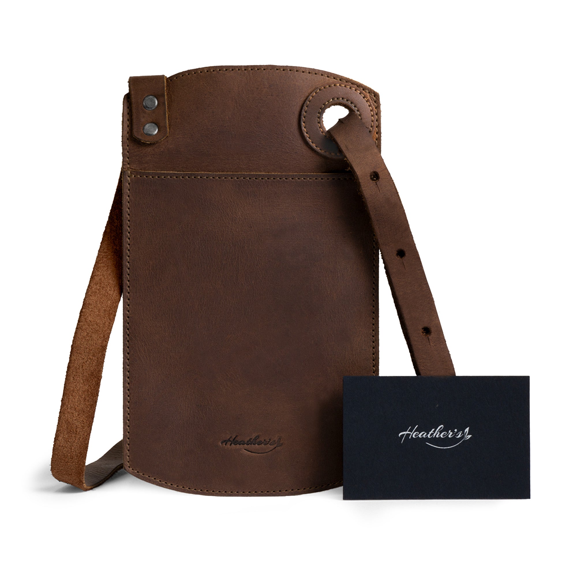 Product shot of the Phone Purse with Adjustable Strap by Heather's, complete with tags highlighting its artisanal quality. Designed for practicality, this horizontal cellphone bag in full grain leather features an adjustable strap and card slot. Handmade in La Antigua Guatemala, this creation showcases the essence of small batch production.