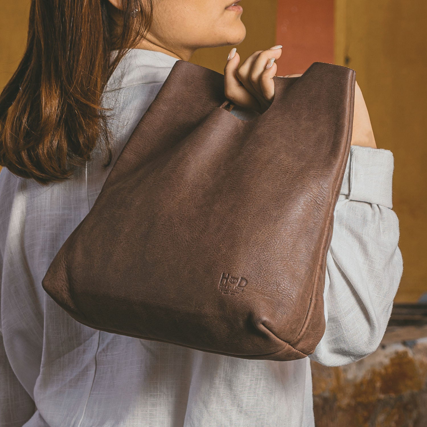 A woman carrying the Hide & Drink Minimalist Boho Handbag on her shoulder, showcasing its elegant design. This minimalist handbag for women is perfect for everyday use, crafted from Full Grain Leather. It embodies rustic charm and is handmade in La Antigua Guatemala & Oaxaca Mexico.