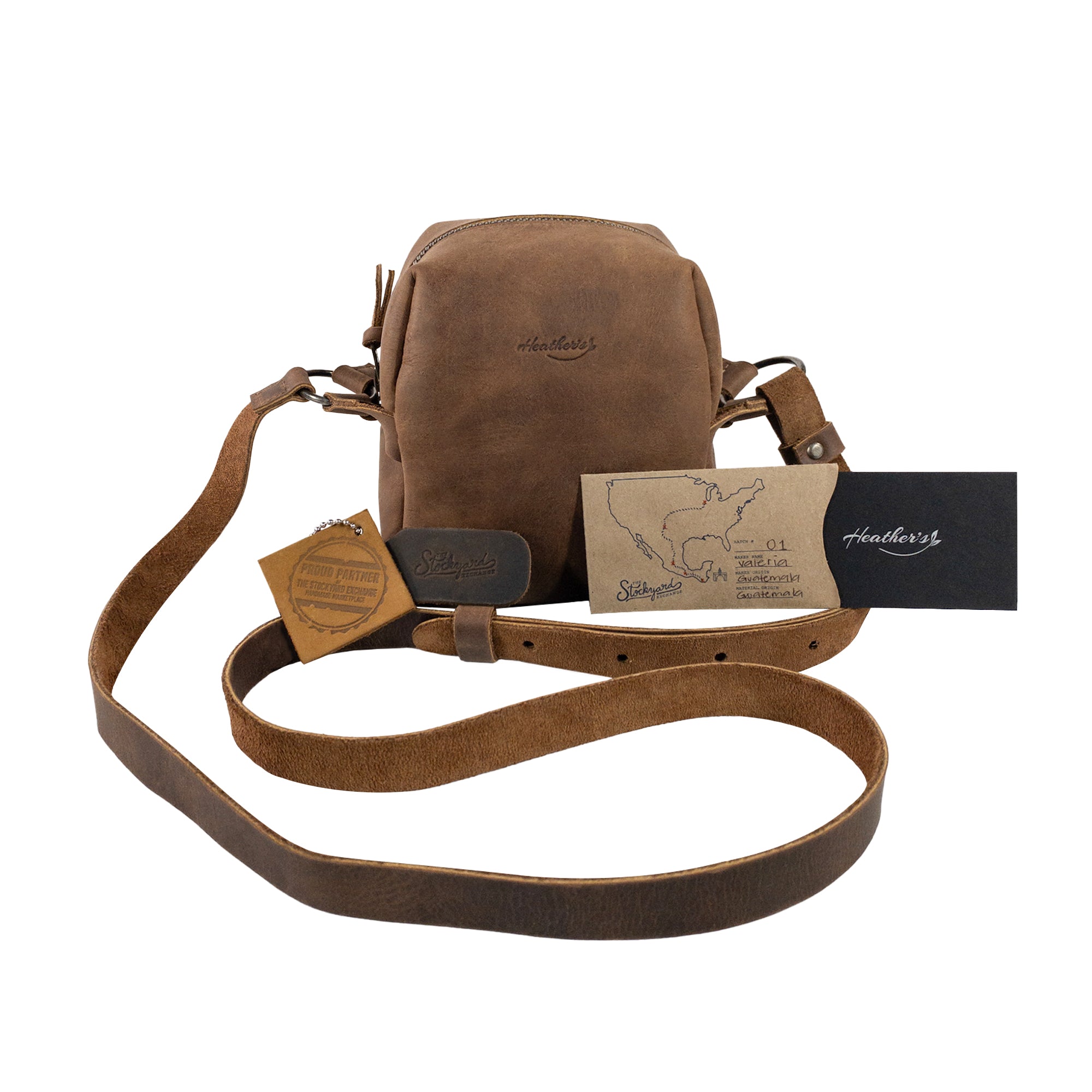 Heather's Cube Shaped Bag displayed with its packaging and tags, reflecting its handmade essence. This Cube Shape Bag with Adjustable Shoulder Strap serves as a delightful Rustic Satchel, perfect as a Handbag or Purse made of exquisite Full Grain Leather. It highlights StockyardX's dedication to Small Batch Production, featuring Hand Cut and Hand Sewn artistry, Fire Branded for authenticity, and is Handmade in La Antigua Guatemala & Oaxaca Mexico.