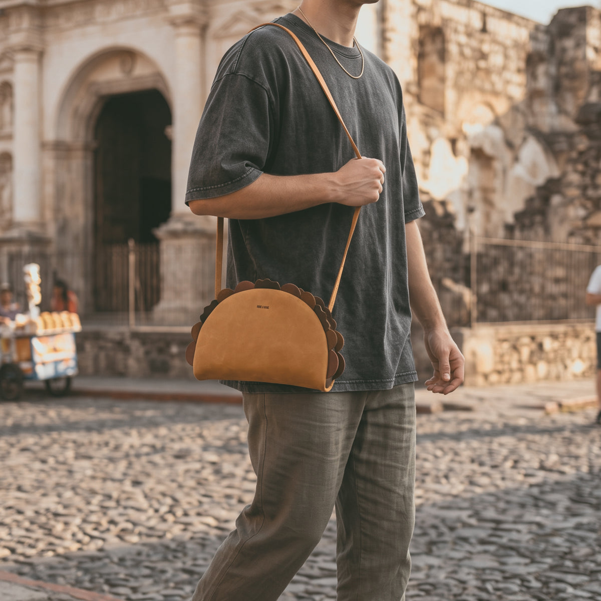 Woman wearing the Hide & Drink Taco Shoulder Bag crossbody in a sunny park, featuring a Full Grain Leather Taco Shoulder Bag with Adjustable Shoulder Strap, Messenger Bag, Crossbody Bag, Zippered Sling Bags, Travel Backpack, Purses for Men and Women, Satchel, StockyardX, Small Batch Production, Hand Cut, Hand Sewn, Fire Branded, Artisan, Handmade in La Antigua Guatemala & Oaxaca Mexico.