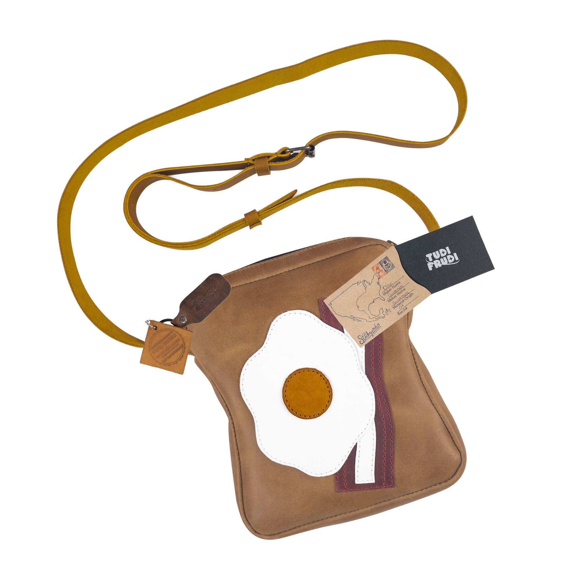The Egg and Bacon Sandwich-Shaped Shoulder Bag by Tudi Frudi, adorned with tags highlighting its artisan craftsmanship. This versatile Handbag, Crossbody Bag, or Messenger Bag is made from Full Grain Leather, emphasizing small batch production techniques, Handmade in La Antigua Guatemala & Oaxaca Mexico.
