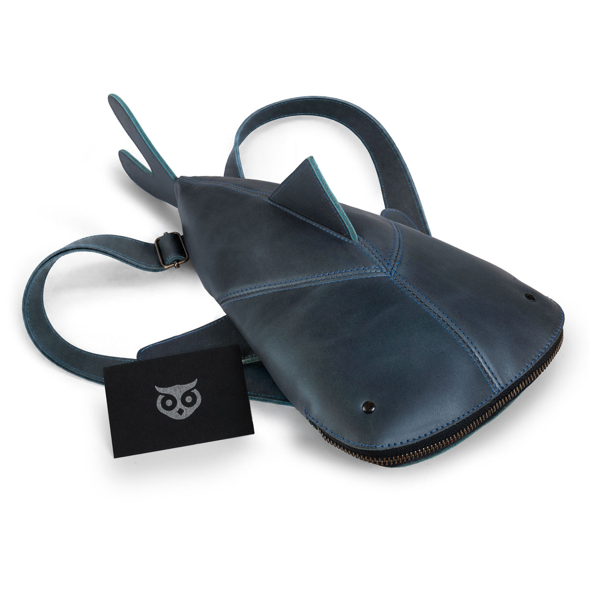 Hide & Drink Leather Shark Backpack (Megalodon) shown flat with detachable-style straps, zipper closure, shark fins, and branded hang tag. Leather Shark Backpack (Megalodon), Casual Bag, Messenger Bag, Travel Bag for Men and Women, Full Grain Leather, StockyardX, Small Batch Production, Hand Cut, Hand Sewn, Fire Branded, Artisan, Handmade in La Antigua Guatemala & Oaxaca Mexico.