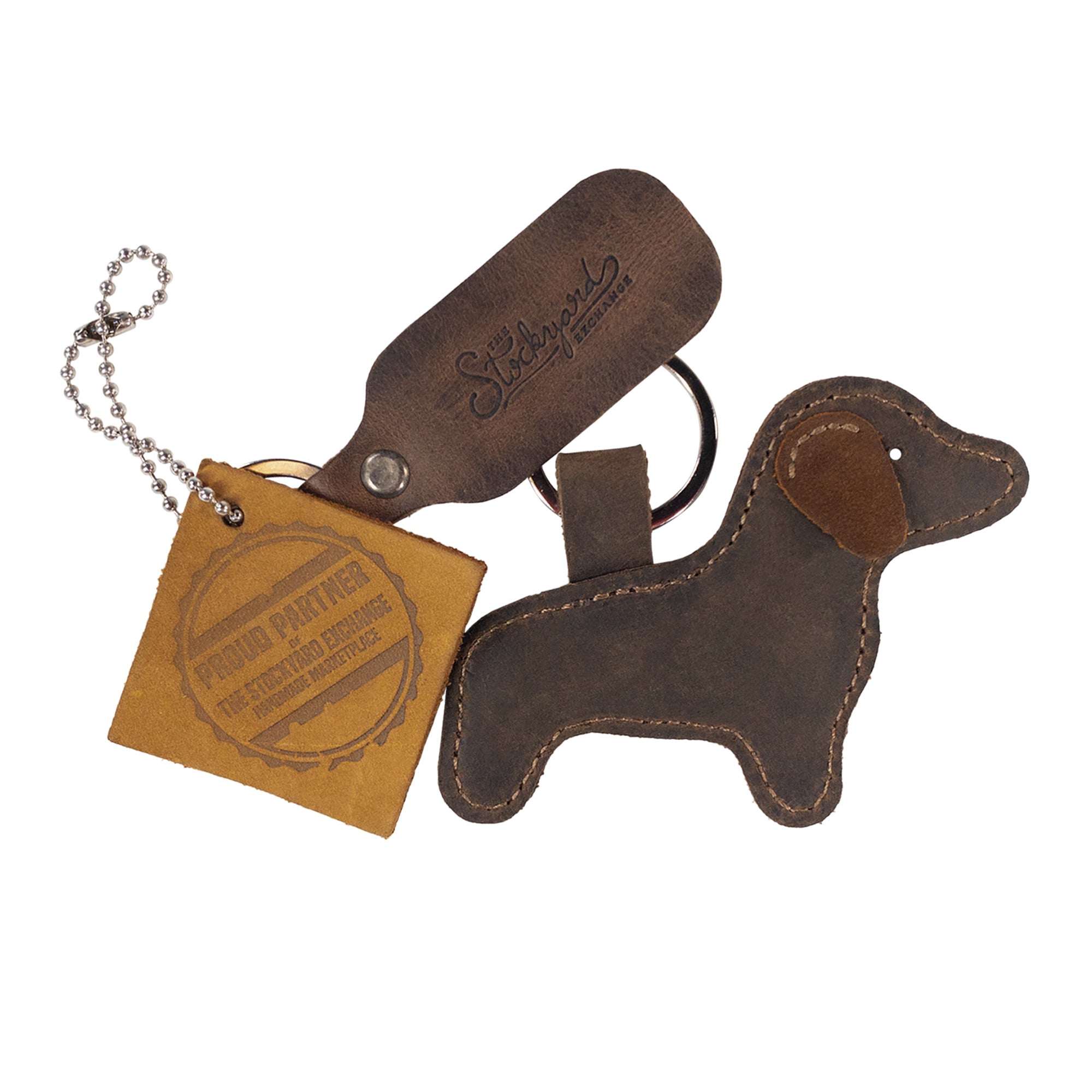 The Hide & Drink Dog Keychain is beautifully displayed alongside branding materials, showcasing its quality. This cute dog-shaped keyring is made from Full Grain Leather and represents the artisan, handmade ethos, produced in small batches in La Antigua Guatemala & Oaxaca Mexico.