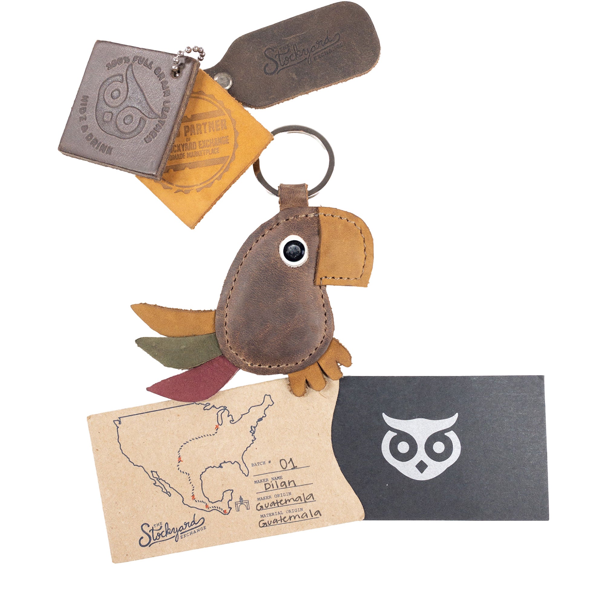 Hide & Drink's Toucan Keychain displayed with accompanying care instructions and branding materials. This full grain leather animal-shaped keyring makes for a charming ornament for your backpack or handbag. Handmade in La Antigua Guatemala & Oaxaca Mexico, it features small batch production techniques, such as hand cut and hand sewn artistry.