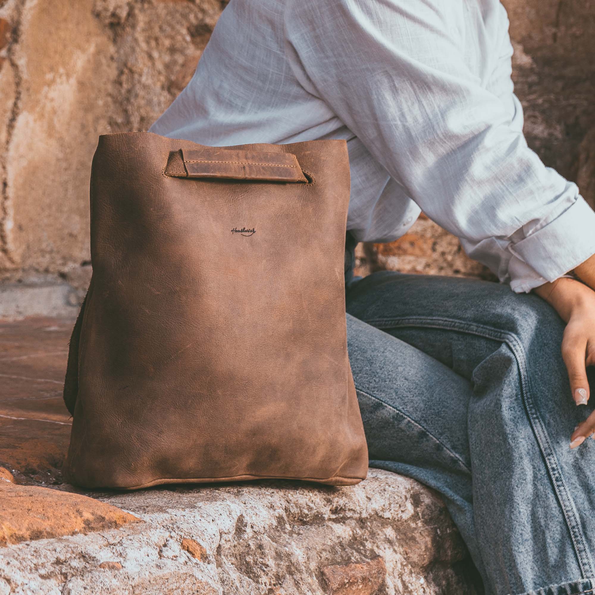 Heather's Convertible Backpack to Shoulder Bag resting next to a seated woman, demonstrating its stylish design and practicality. This spacious crossbody for women is crafted from Full Grain Leather and reflects small batch production and artisan craftsmanship from La Antigua Guatemala & Oaxaca Mexico.