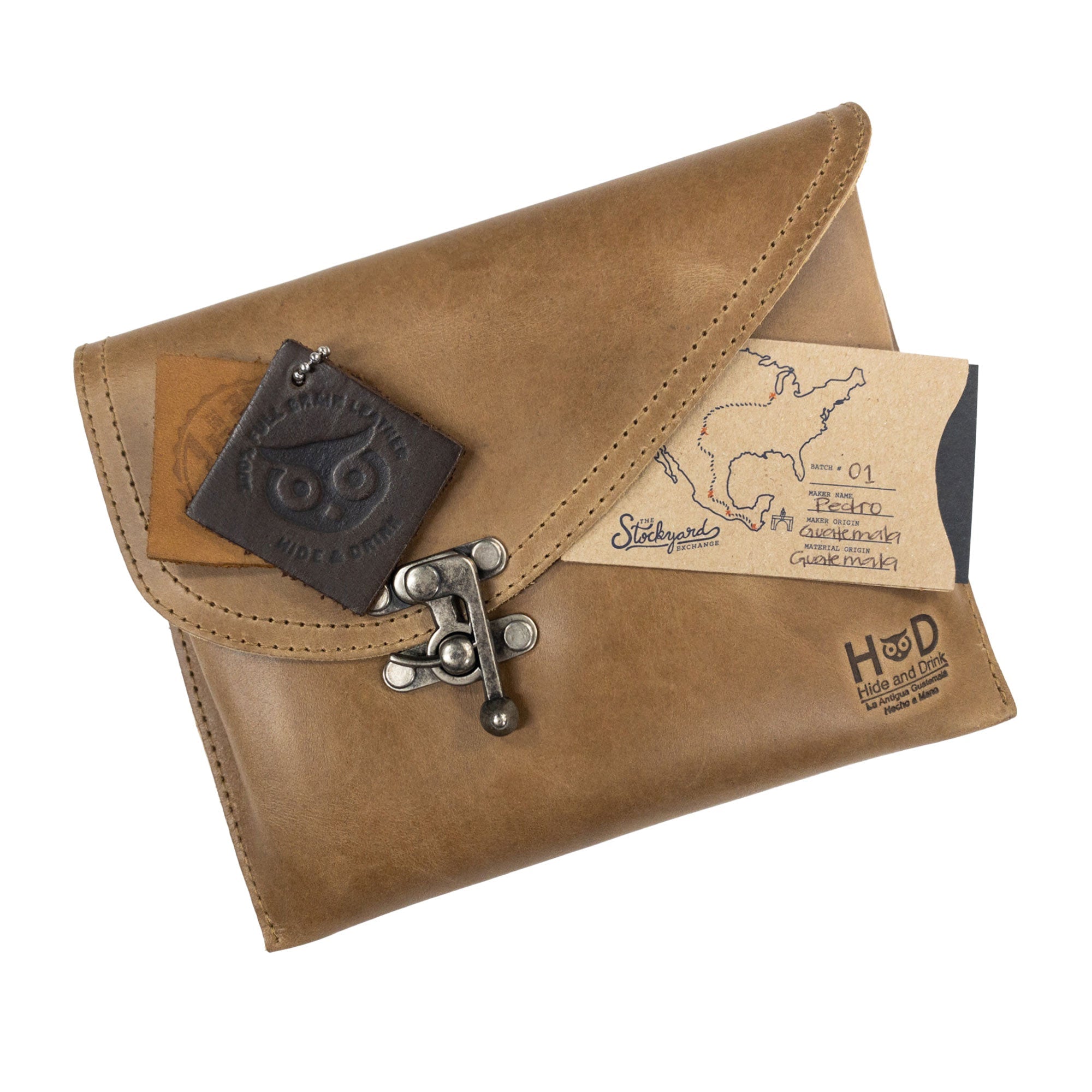 The tan Petite Vintage Clutch Bag by Hide & Drink displayed with personal items, highlighting its style and utility. This chic handbag made from premium full grain leather is perfect as an evening bag or travel accessory, celebrating handmade craftsmanship from La Antigua Guatemala & Oaxaca Mexico.