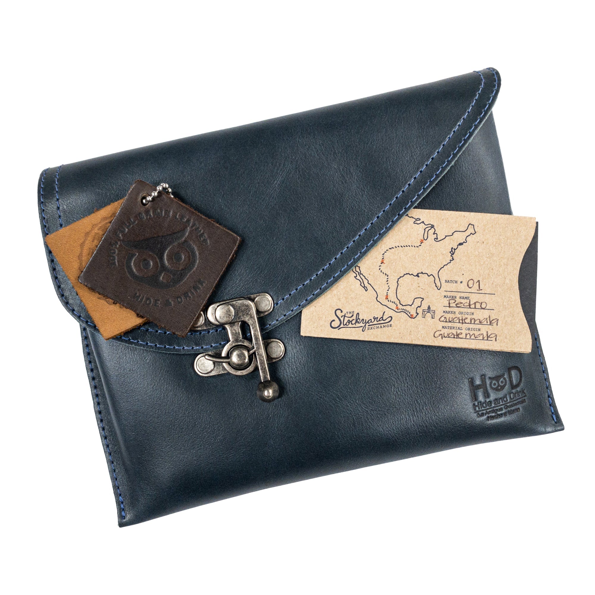The navy Petite Vintage Clutch Bag by Hide & Drink showcased with personal items, highlighting its practical design. Crafted from full grain leather, this evening bag is a perfect travel accessory, embodying the handmade quality from La Antigua Guatemala & Oaxaca Mexico.