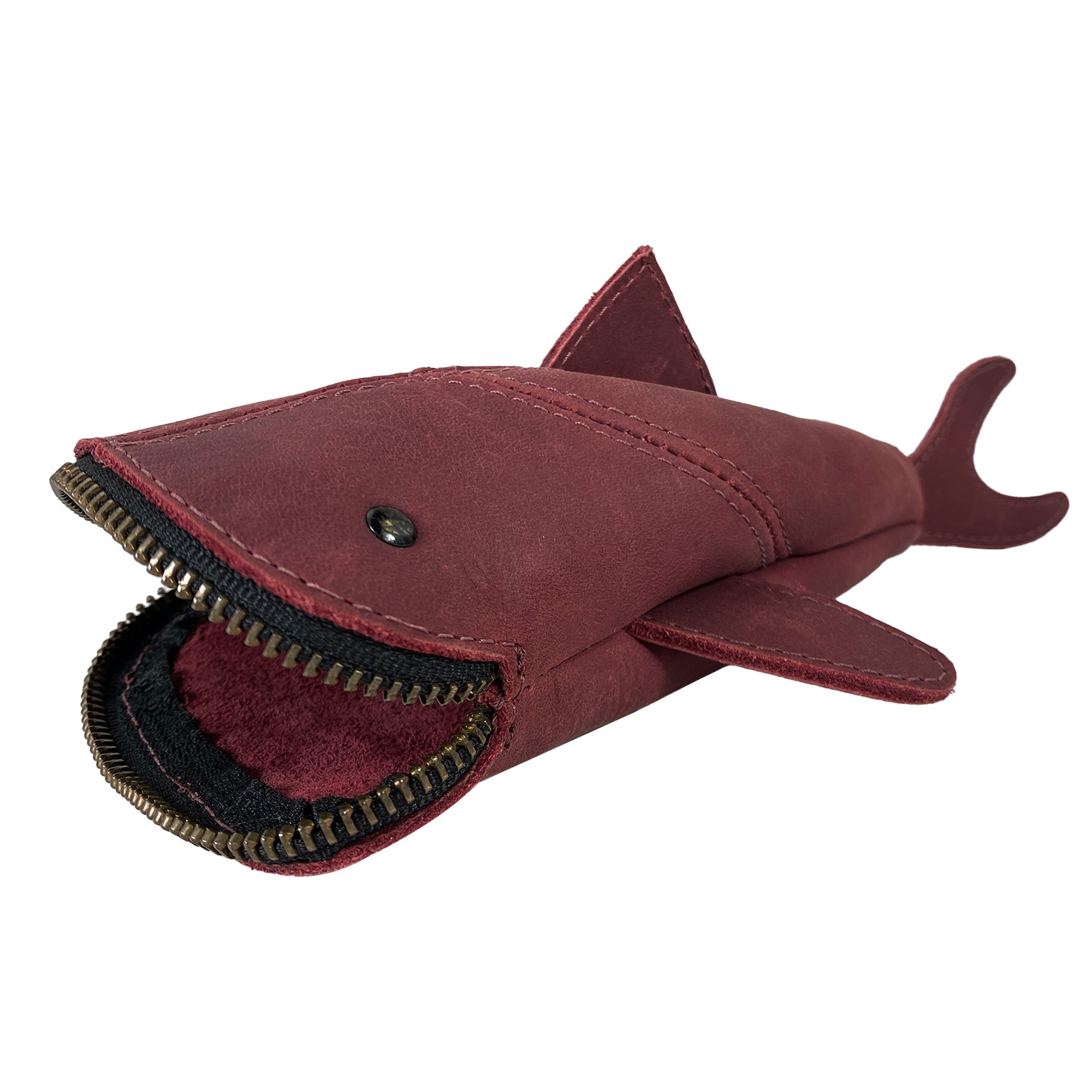 Red leather variant of the Leather Shark Pouch by Hide & Drink, filled with various stationary items. This zippered shark shaped case, suitable for use as a change bag or pencil purse, is crafted from full grain leather and exemplifies artisan quality from La Antigua Guatemala & Oaxaca Mexico with a playful design.