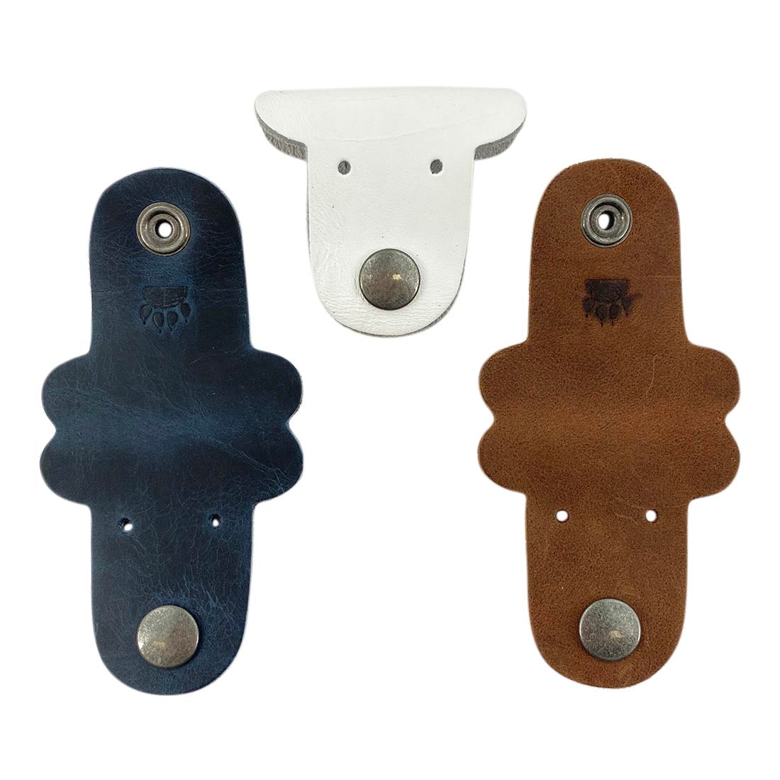 Multicolor Dog Cord Keeper (3 Pack) by Taco Dog displaying three unique dog-shaped leather cord wraps in blue, white, and brown, perfect for keeping your cords neat. Dog Cord Keeper - Wrap Up Your Cables, Earbuds, Headphones, Chargers - Clip The Straps Together for Easy Management and Travel - 3-Pack, Full Grain Leather, StockyardX, Small Batch Production, Hand Cut, Hand Sewn, Fire Branded, Artisan, Handmade in La Antigua Guatemala & Oaxaca Mexico.