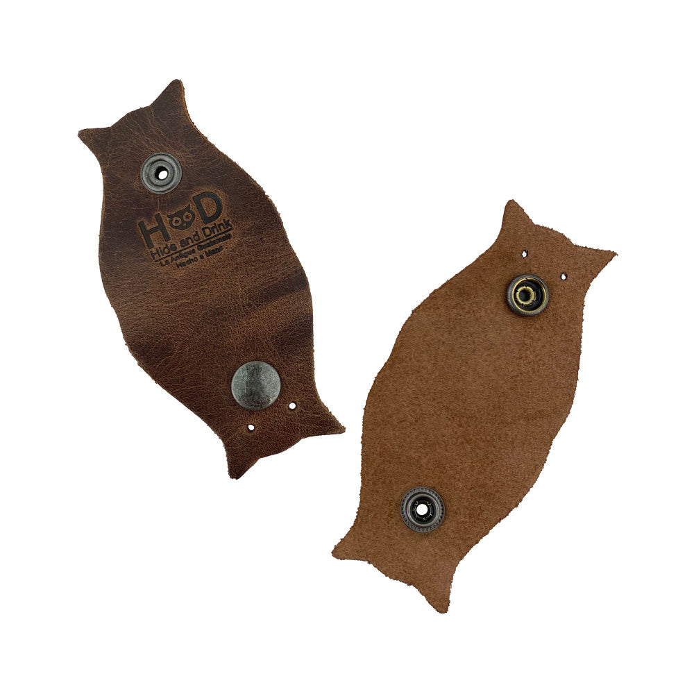 Owl Shaped Cord Keeper (2-Pack) by Hide & Drink featuring high-quality leather in a warm hue, perfect for adding a personal touch to cord management. Owl Shaped Cord Keeper (Cord Clam) 2-Pack. Full Grain Leather, StockyardX, Small Batch Production, Hand Cut, Hand Sewn, Fire Branded, Artisan, Handmade in La Antigua Guatemala & Oaxaca Mexico.
