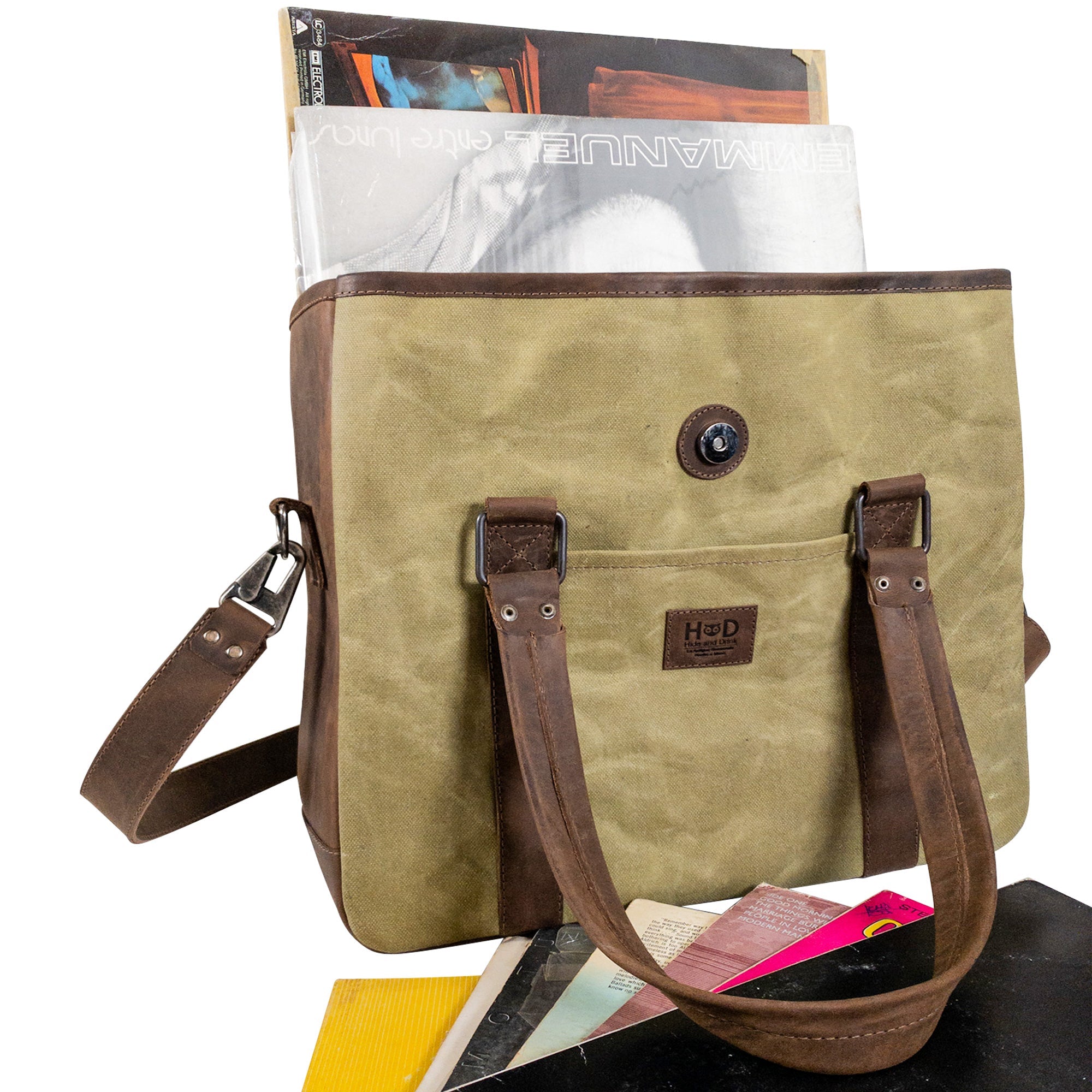 The Vinyl Records Messenger Bag by Hide & Drink, filled with records and accessories, perfect for music enthusiasts. This artisan-crafted bag from La Antigua Guatemala & Oaxaca Mexico, combines waxed canvas and full grain leather for a unique travel solution.