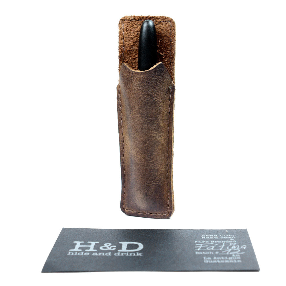 Hide & Drink Fisher Space Pen Case, showcasing a stylish office accessory holding a pen. This rustic individual sleeve is crafted from high-quality full grain leather, perfect for 3.75 in. adjustable pens. Handmade and fire branded by artisans in La Antigua Guatemala and Oaxaca Mexico, it encapsulates small batch production and artisan craftsmanship.